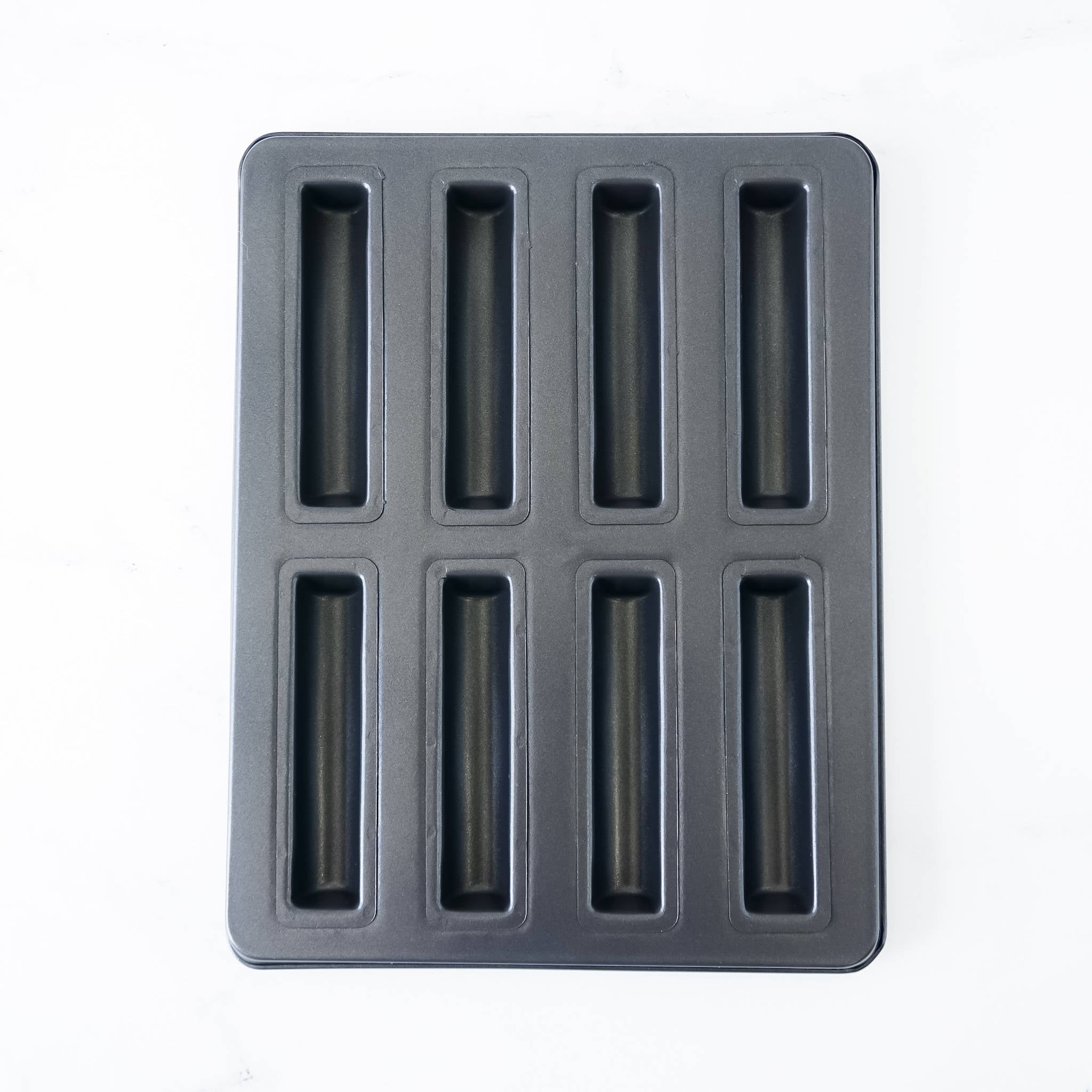 A black financier cake pan with eight cavities, each shaped like a baton. The pan is made of cold-rolled steel with a nonstick coating.