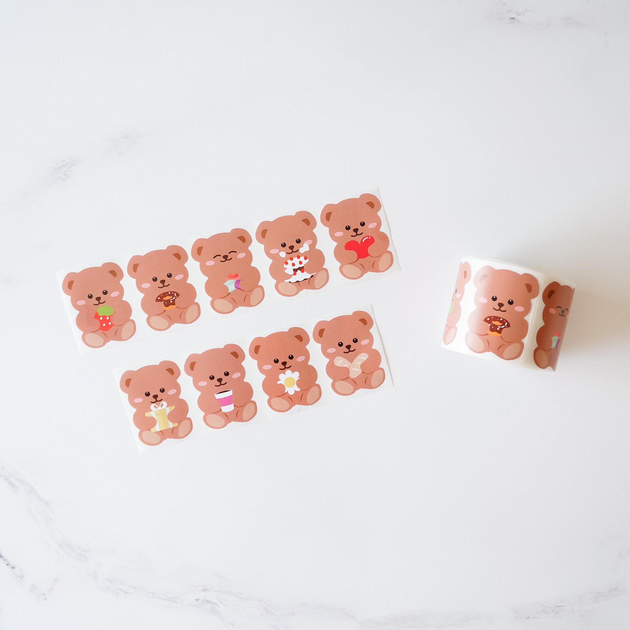 A collection of bear-shaped stickers in various designs, placed on a light surface, with a roll of stickers partially unrolled.