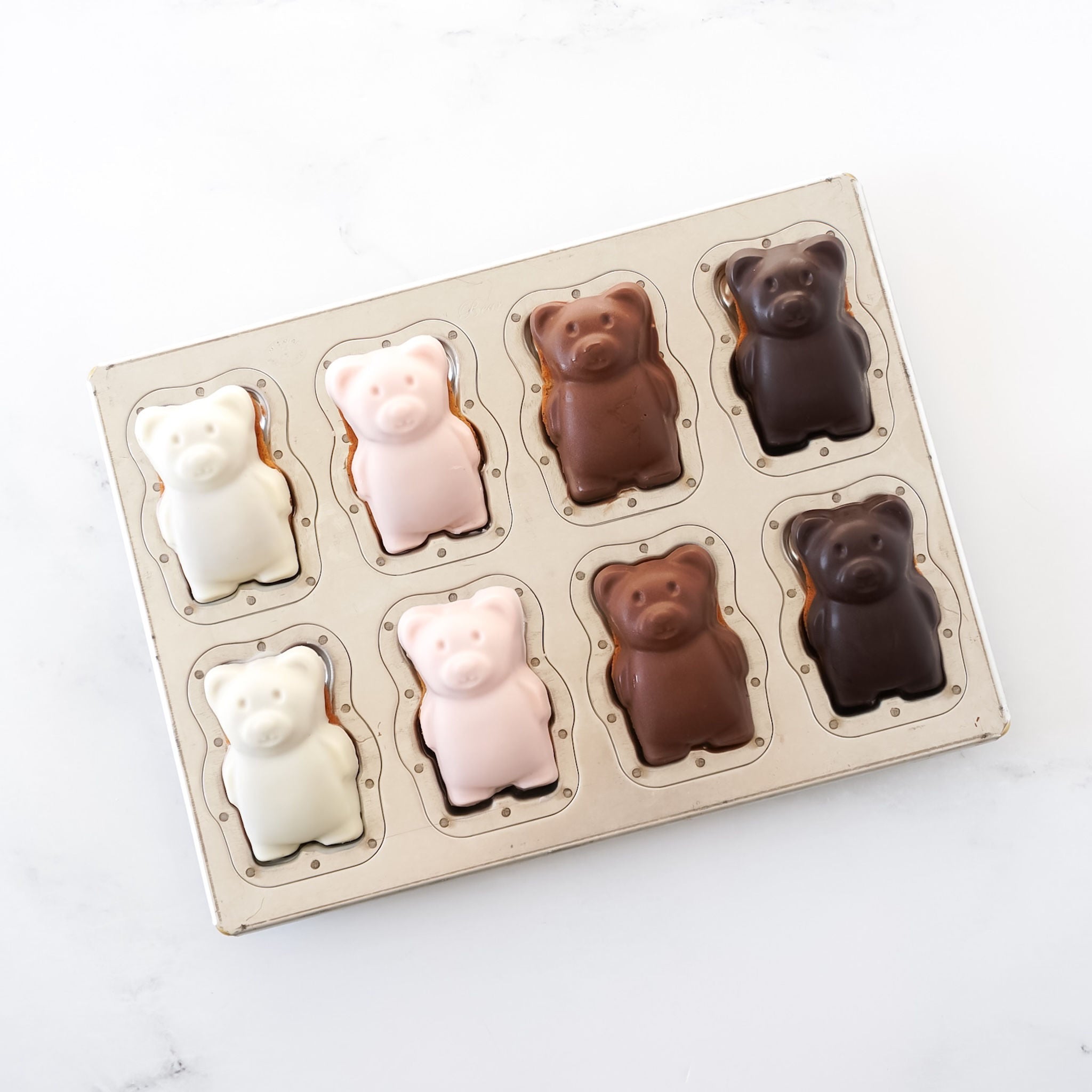 A silicone-coated madeleine pan with bear shapes for baking, displaying various shades of chocolate coated madeleines, 