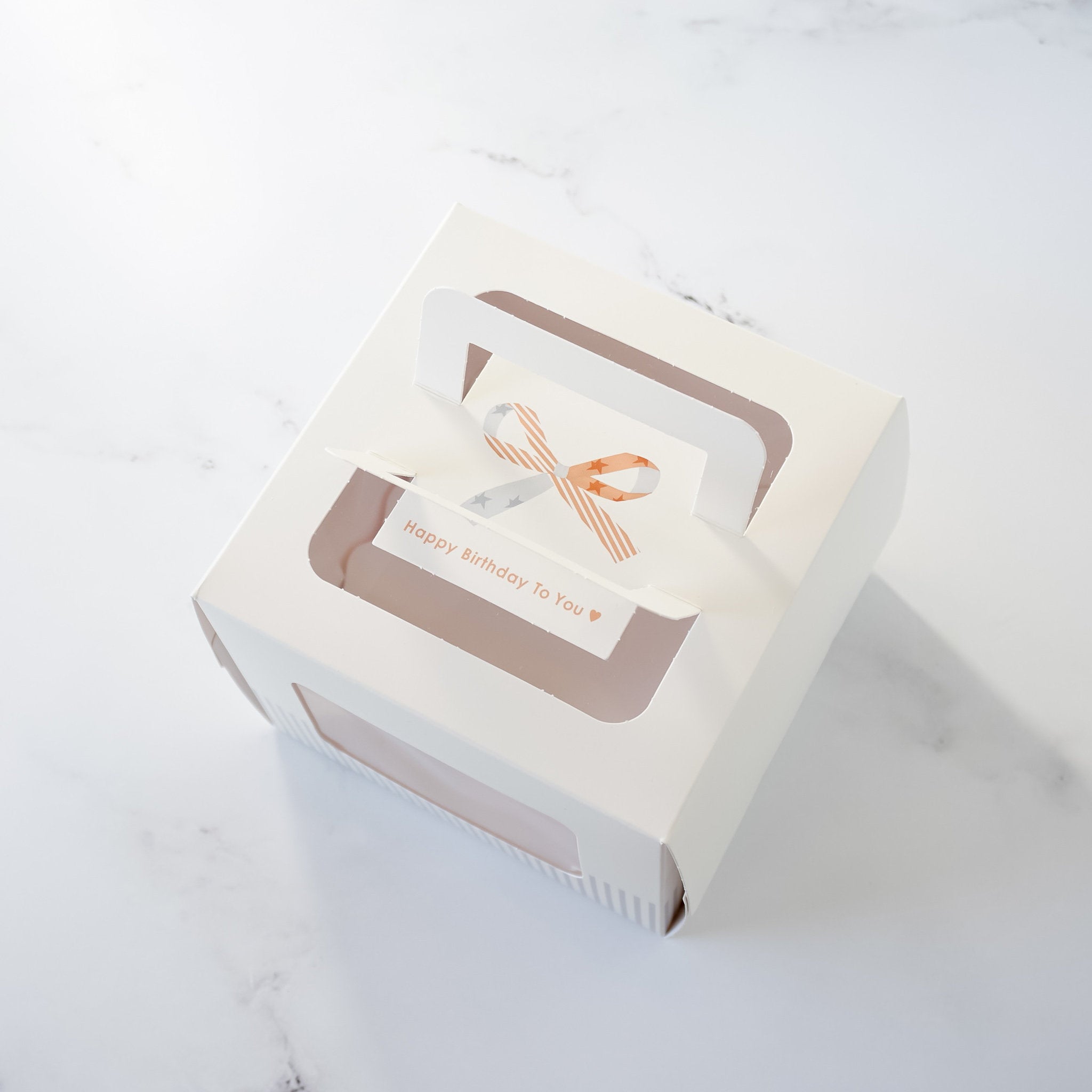 A white cardboard box with a clear window and a handle. The box has a message on it that says &