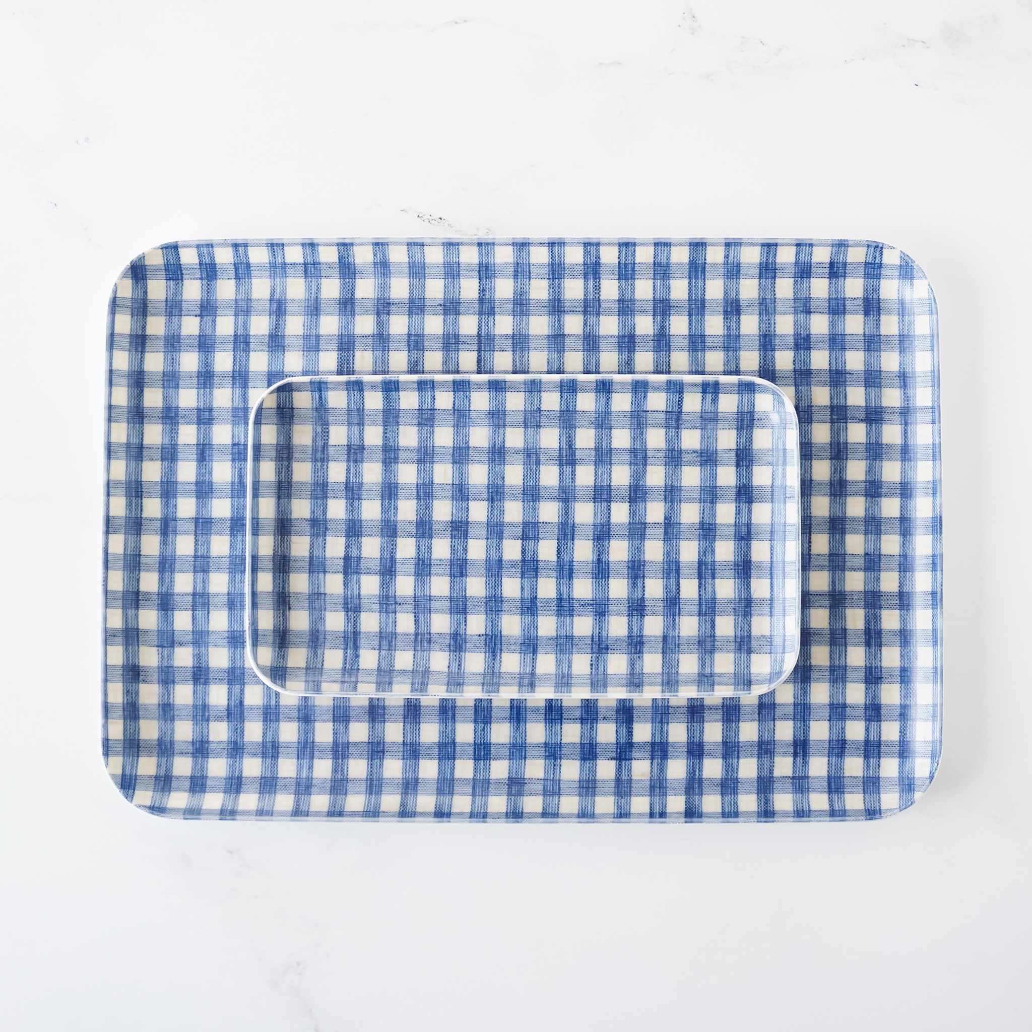 Two rectangular blue and white gingham linen coated trays, one inside the other, on a white background.