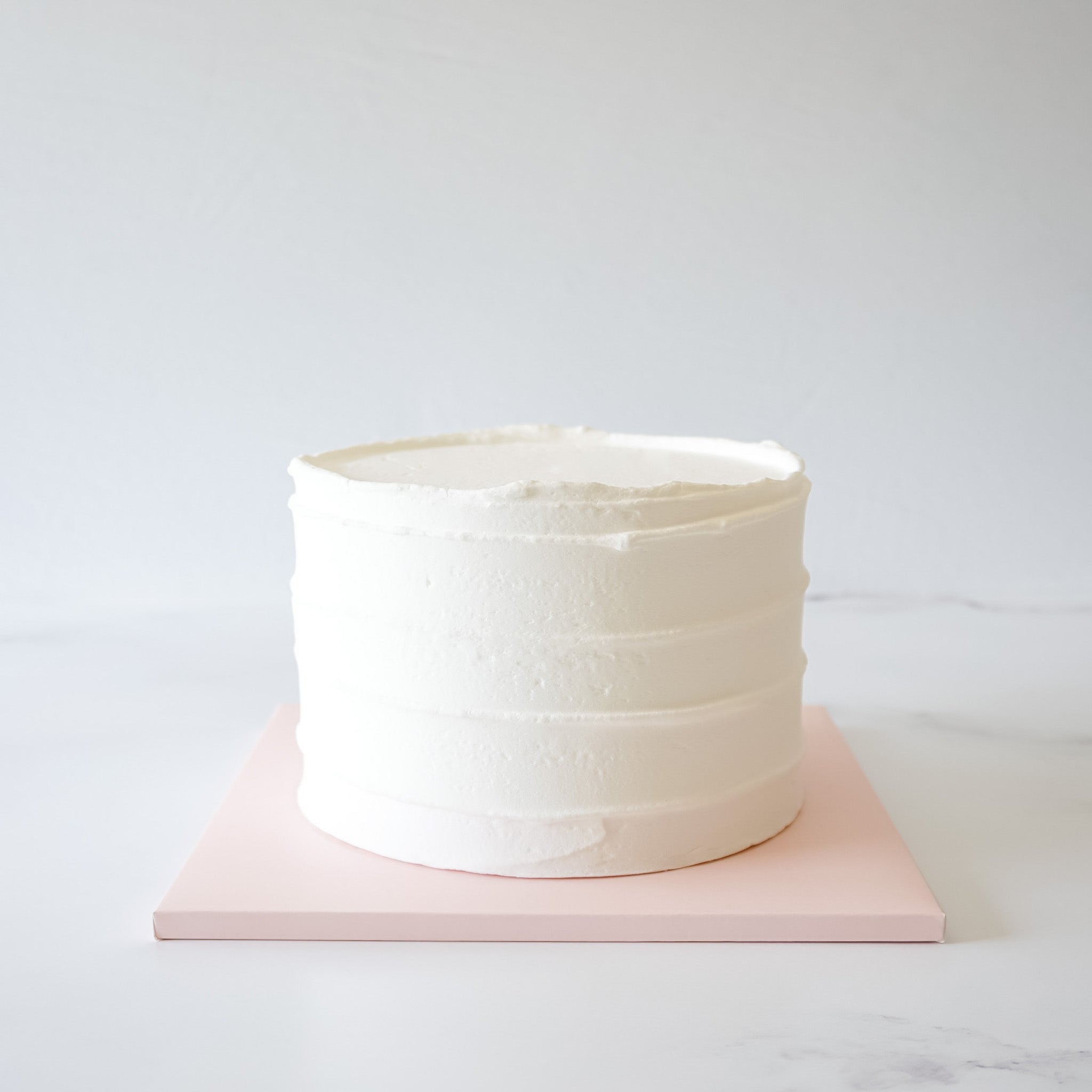 A blush pink cake board with a matte finish, displaying a frosted cake.