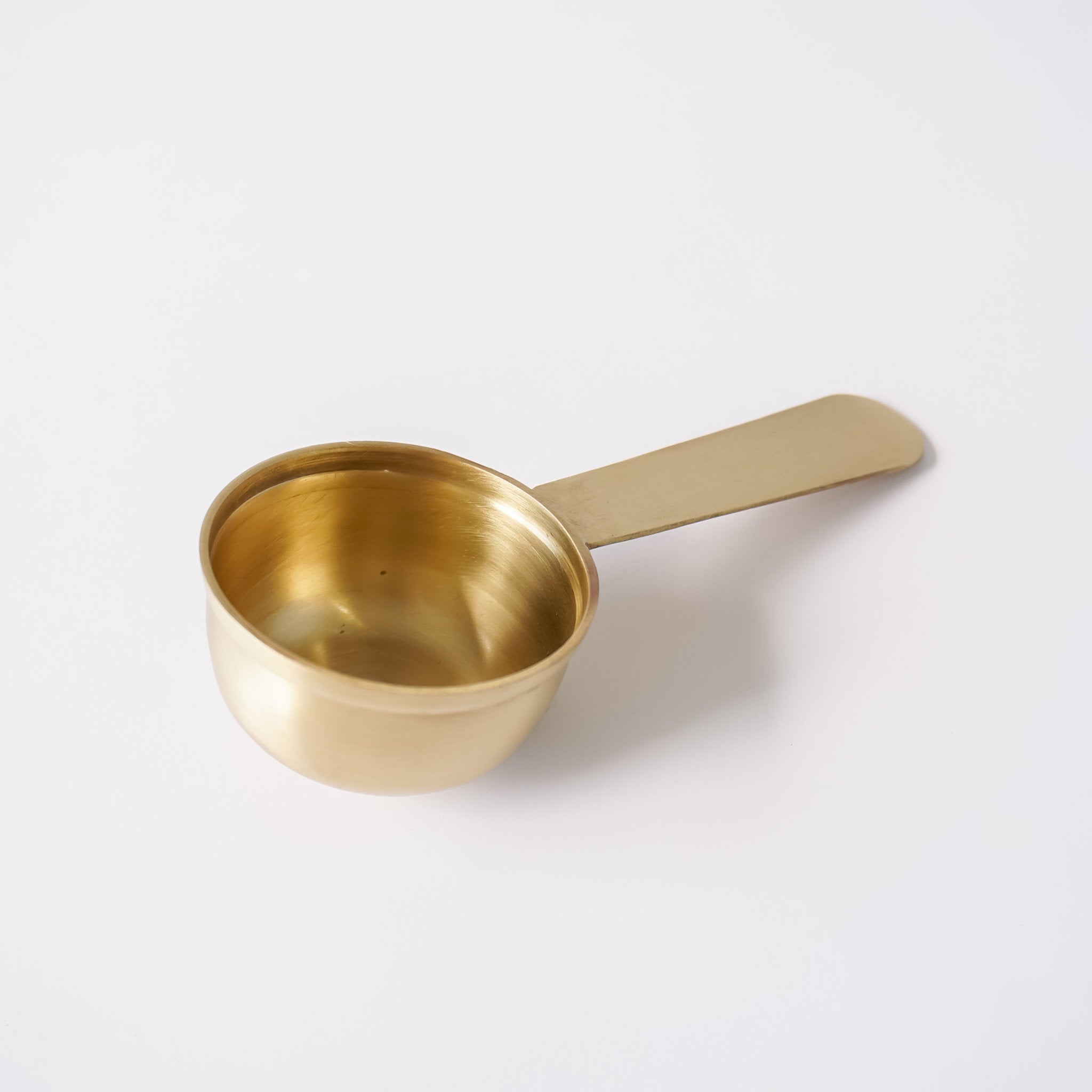 A small brass measuring spoon with a flat handle, shown on a clean white background.