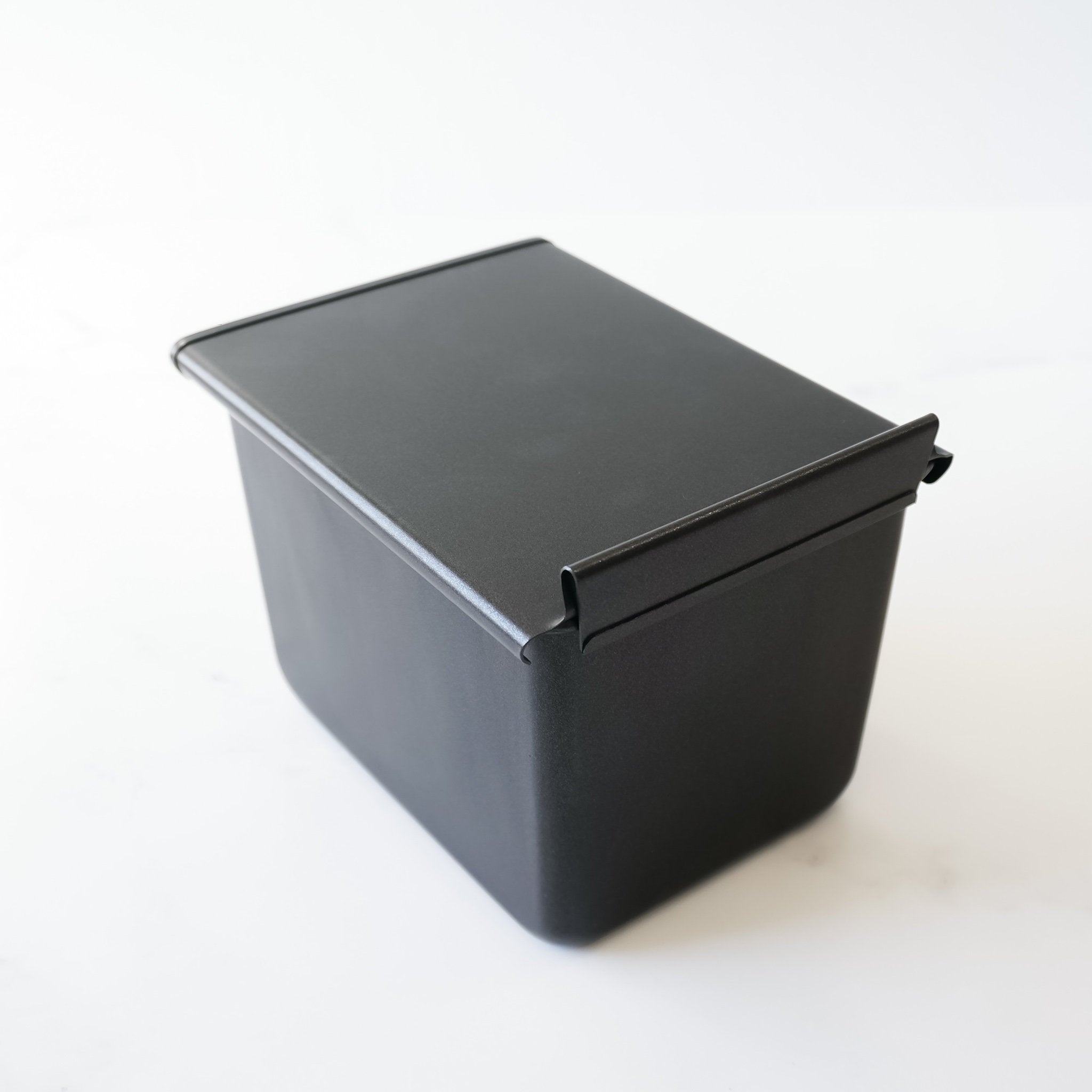 A black metal bread loaf pan with a hinged lid. The pan is rectangular and has a smooth, matte finish.