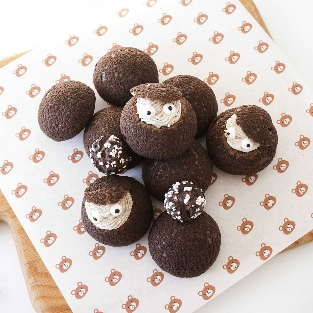 Chocolate cream puffs with faces on a white surface with teddy bear pattern