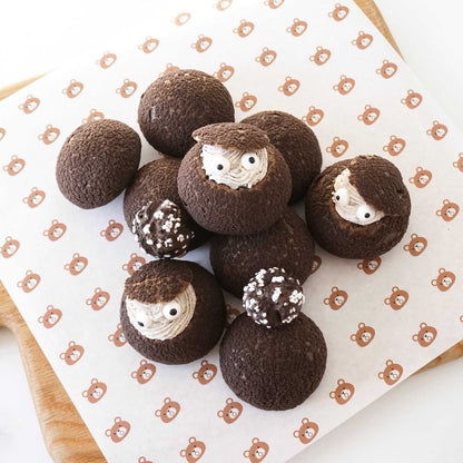 Chocolate cream puffs with faces on a white surface with teddy bear pattern