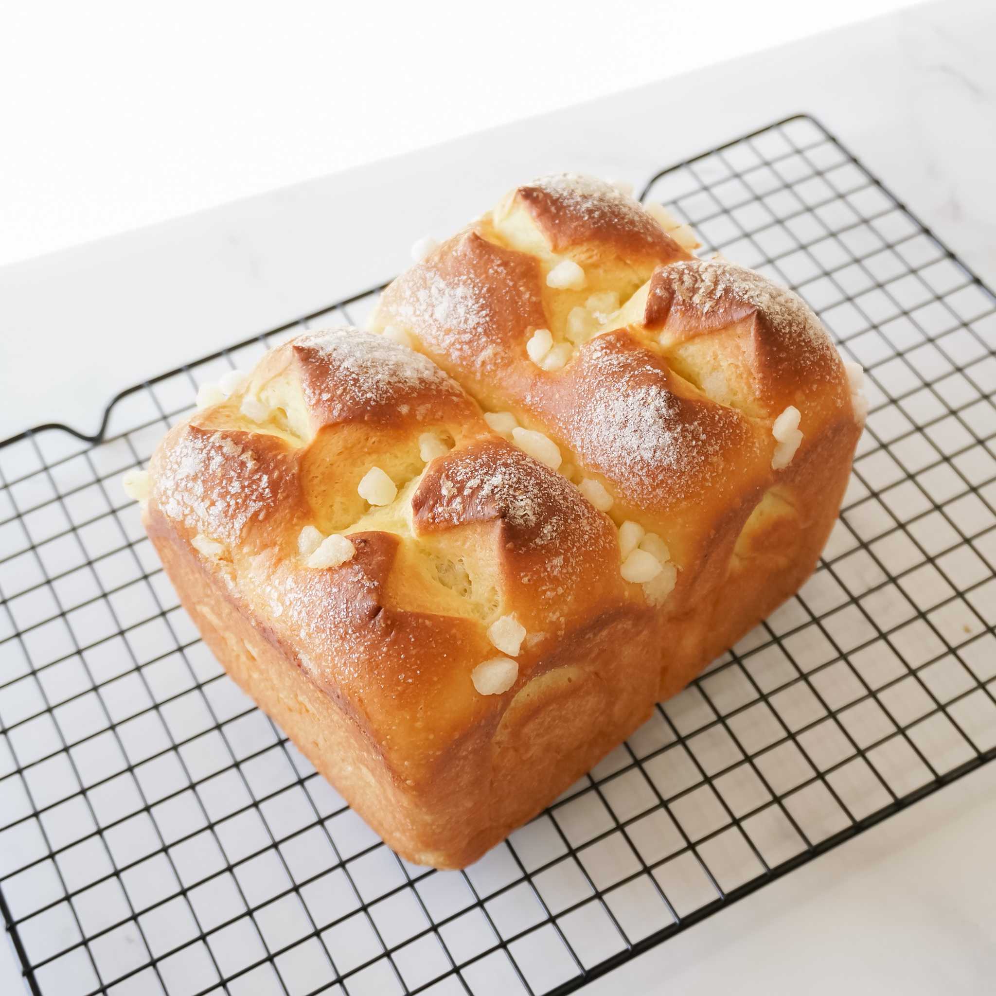 A loaf of brioche bread with a golden brown crust, topped with sugar crystals and dusted with powdered sugar. The bread is sitting on a black wire rack.