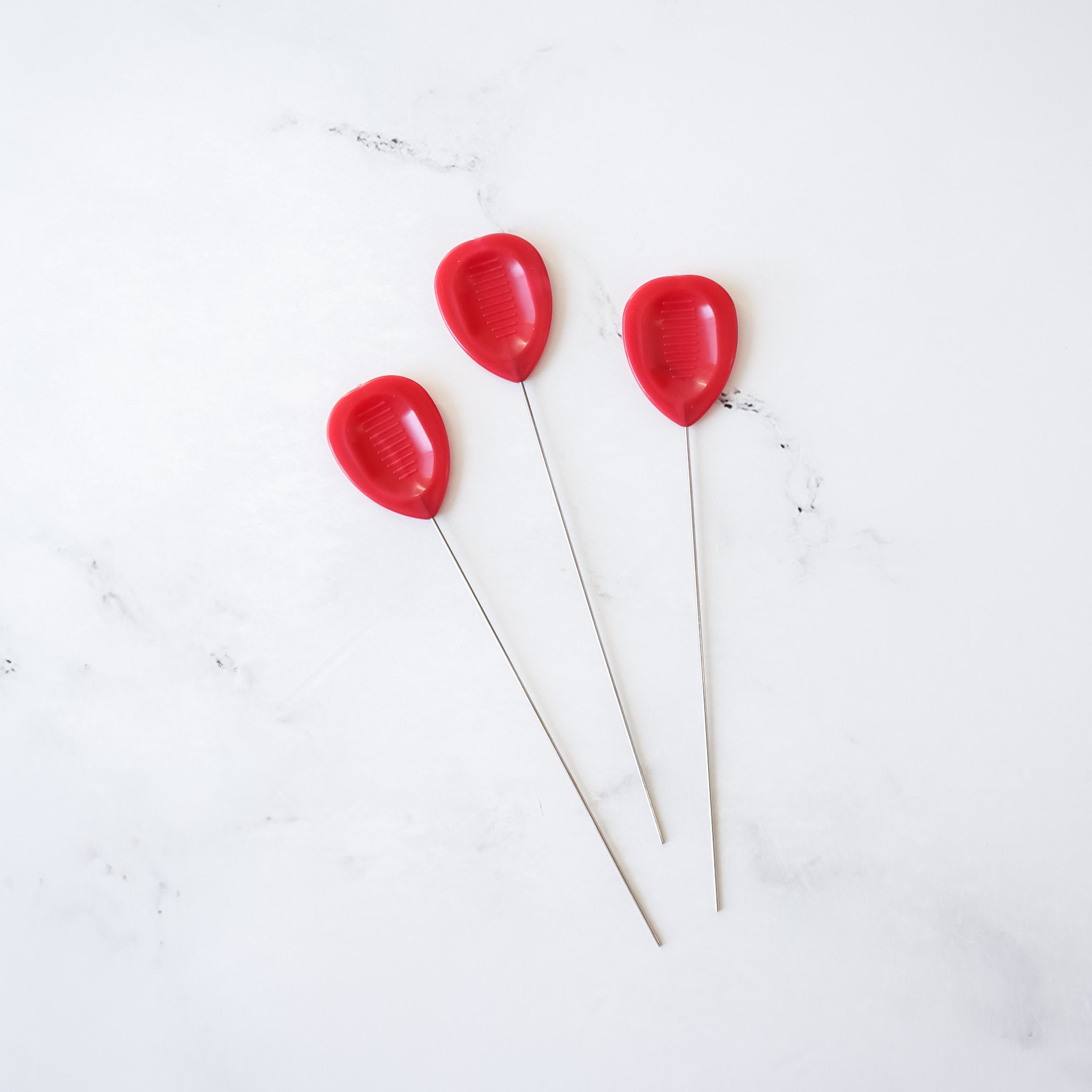 Three red cake testers with stainless steel handles on a white background.