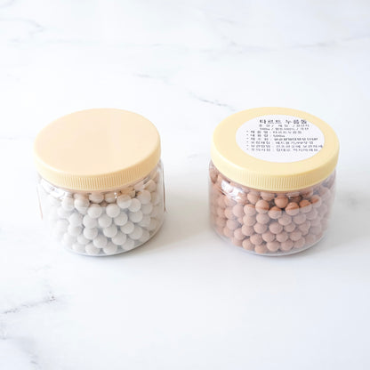 Two jars with beige lids containing white and red clay pie weights on a white background