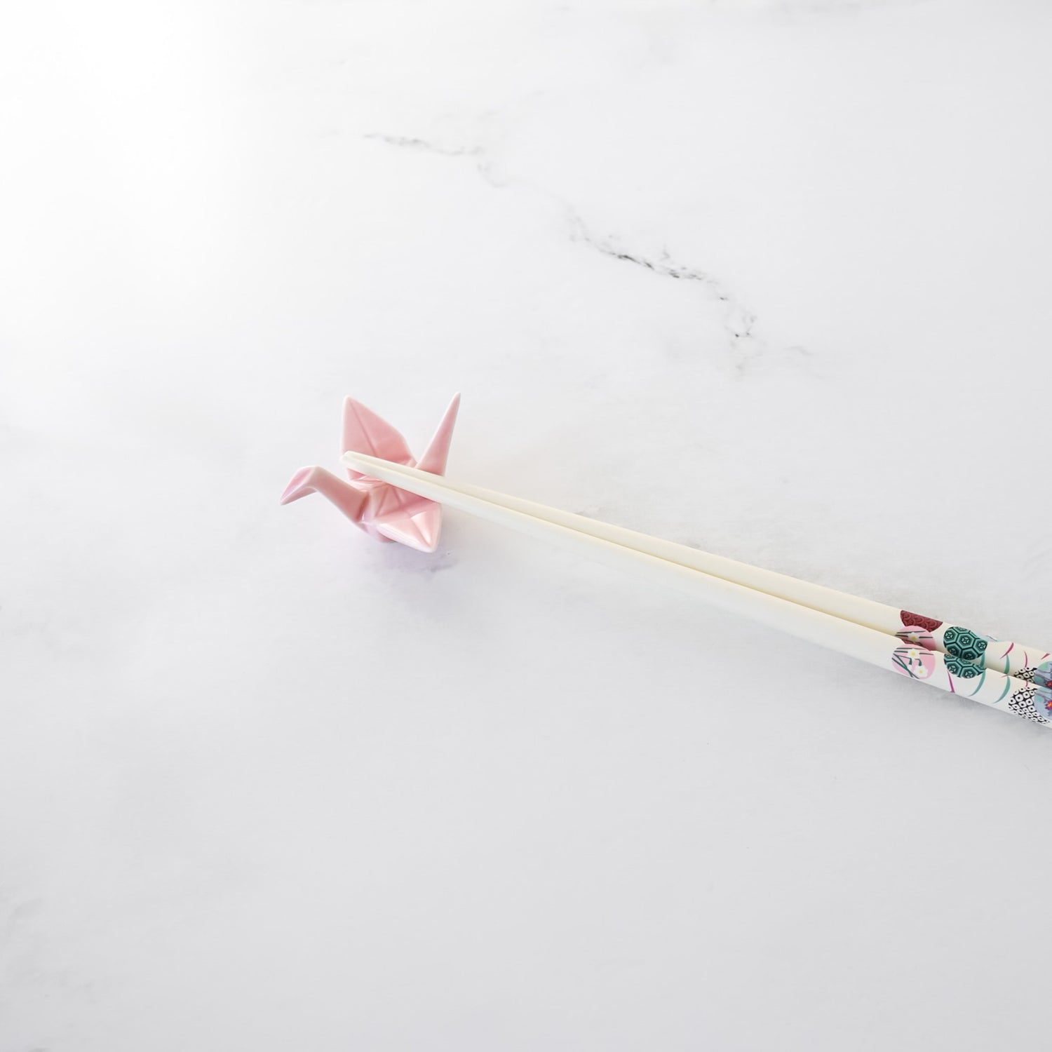 Pink origami crane chopstick rest with white chopsticks on a white marble surface