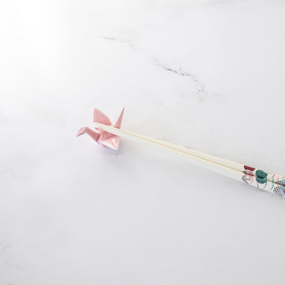 Pink origami crane chopstick rest with white chopsticks on a white marble surface
