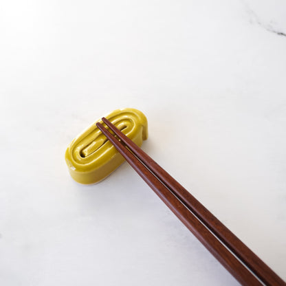 Yellow tamagoyaki chopstick rest with wooden chopsticks on a white background