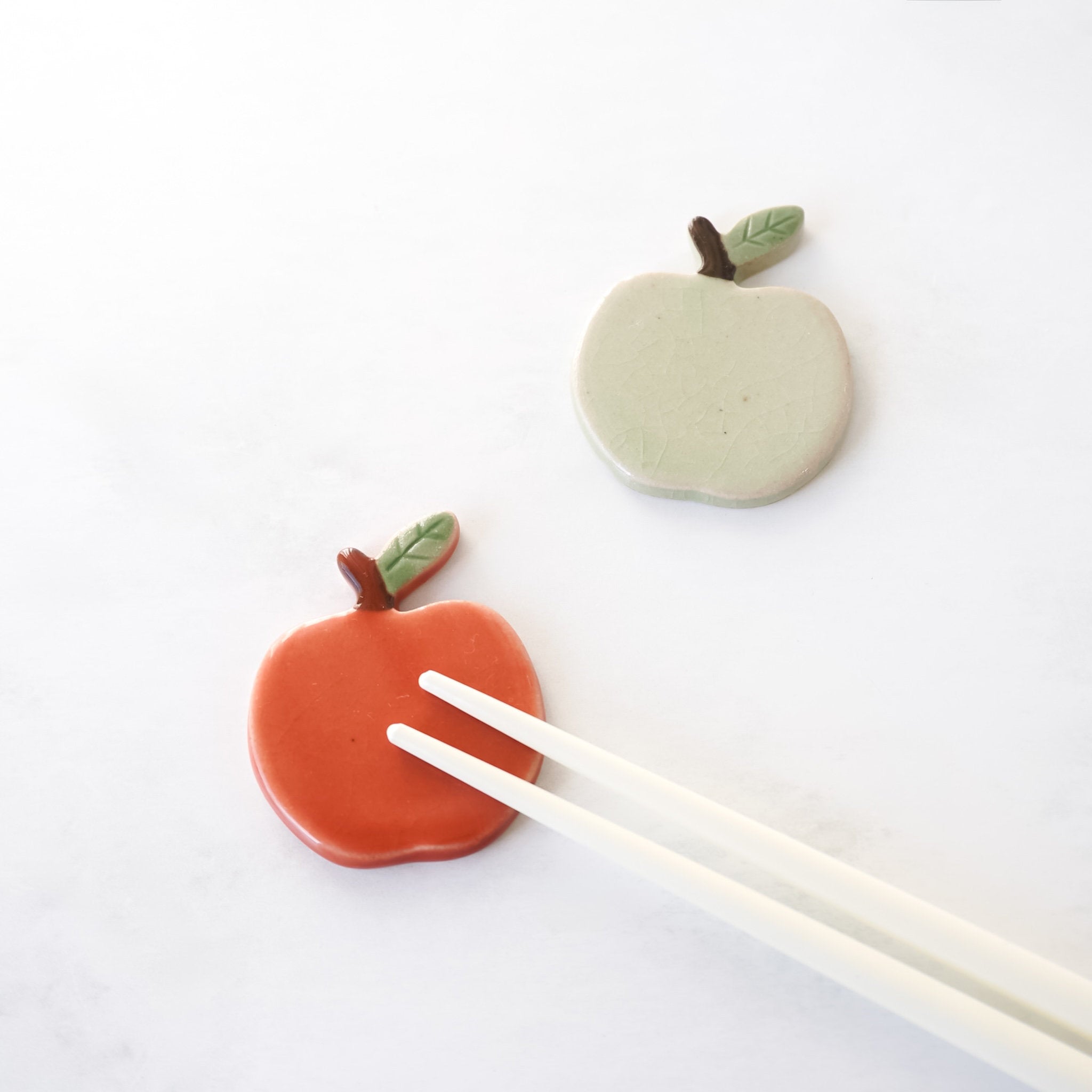 Two ceramic apple-shaped chopstick rests with leaves on a white background