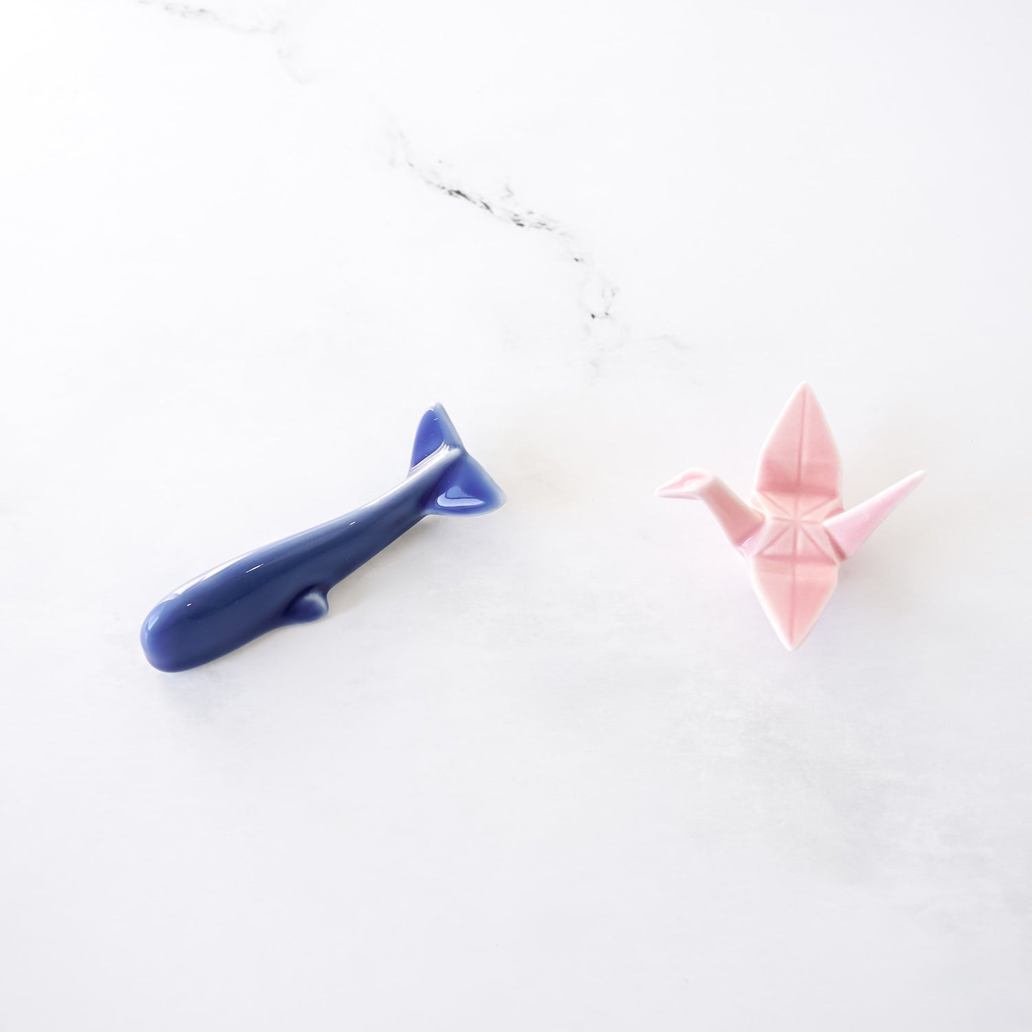 Blue whale and pink origami crane chopstick rests on a white background