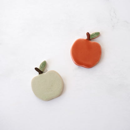 Two clay apple-shaped chopstick rests on a white background
