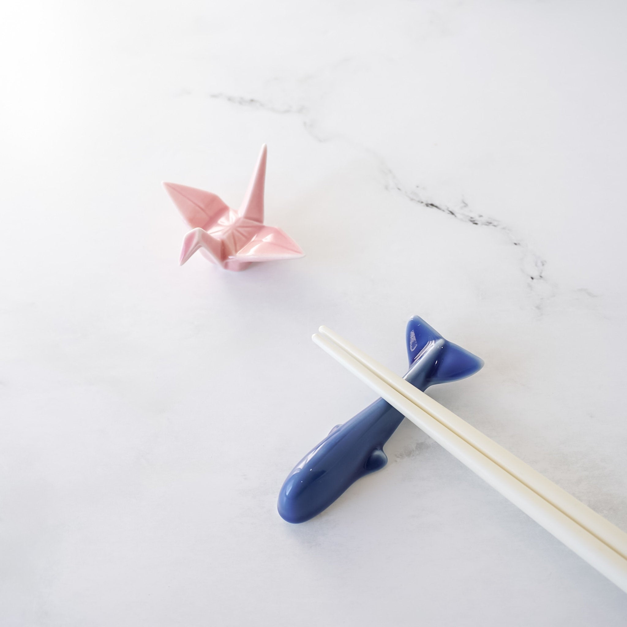 Blue whale chopstick rest with pink origami crane on a white marble surface