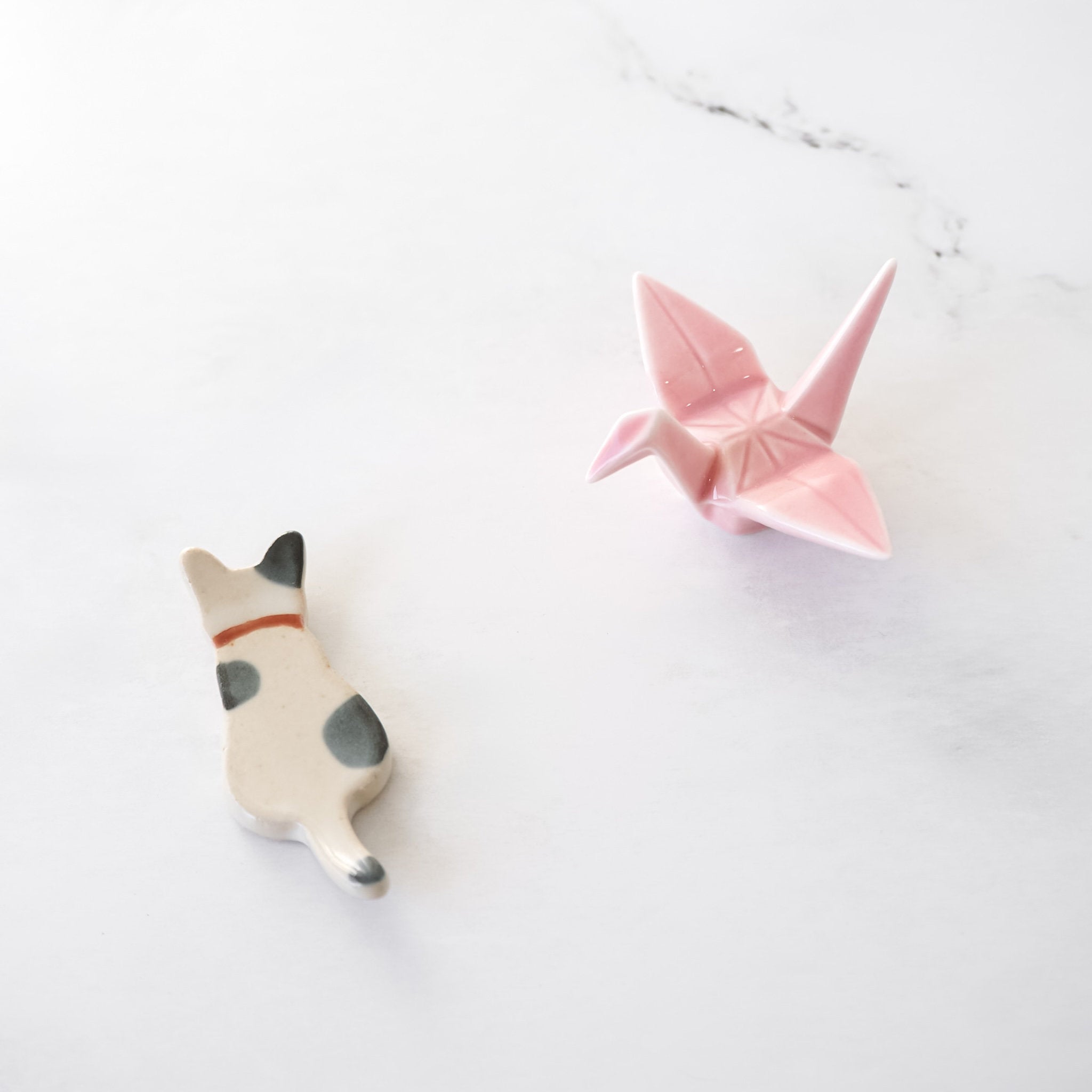 Pink origami crane and ceramic cat chopstick rests on a white surface