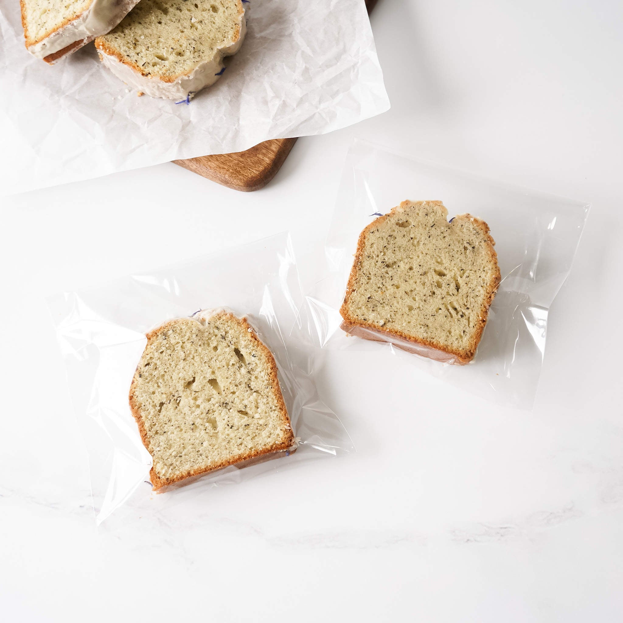 Two slices of Earl Grey pound cake are individually packaged in clear plastic bags. The cake is light brown with a light beige glaze and visible Earl Grey tea.