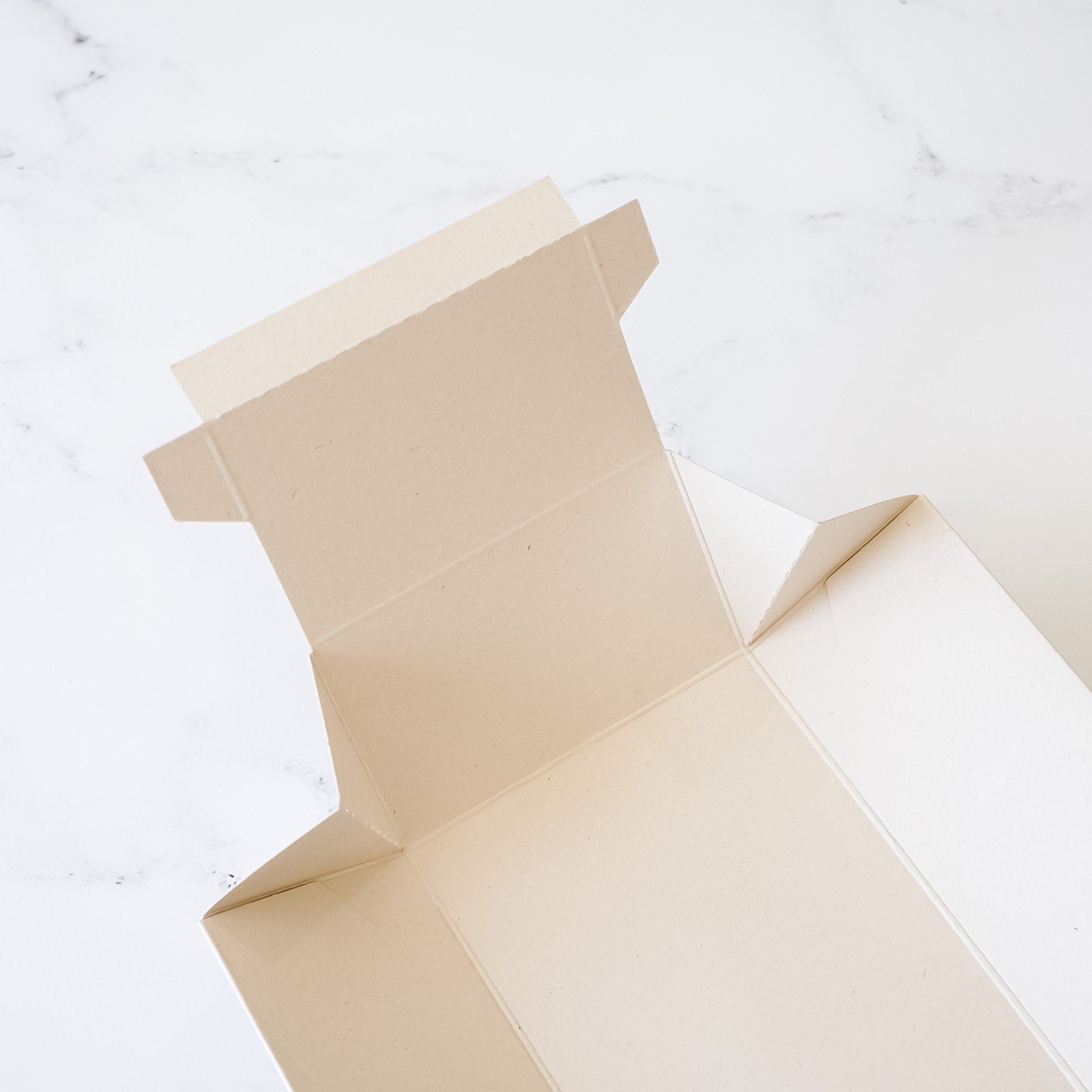 A light beige cardboard box with a folded top flap. The box is empty and ready to be filled.