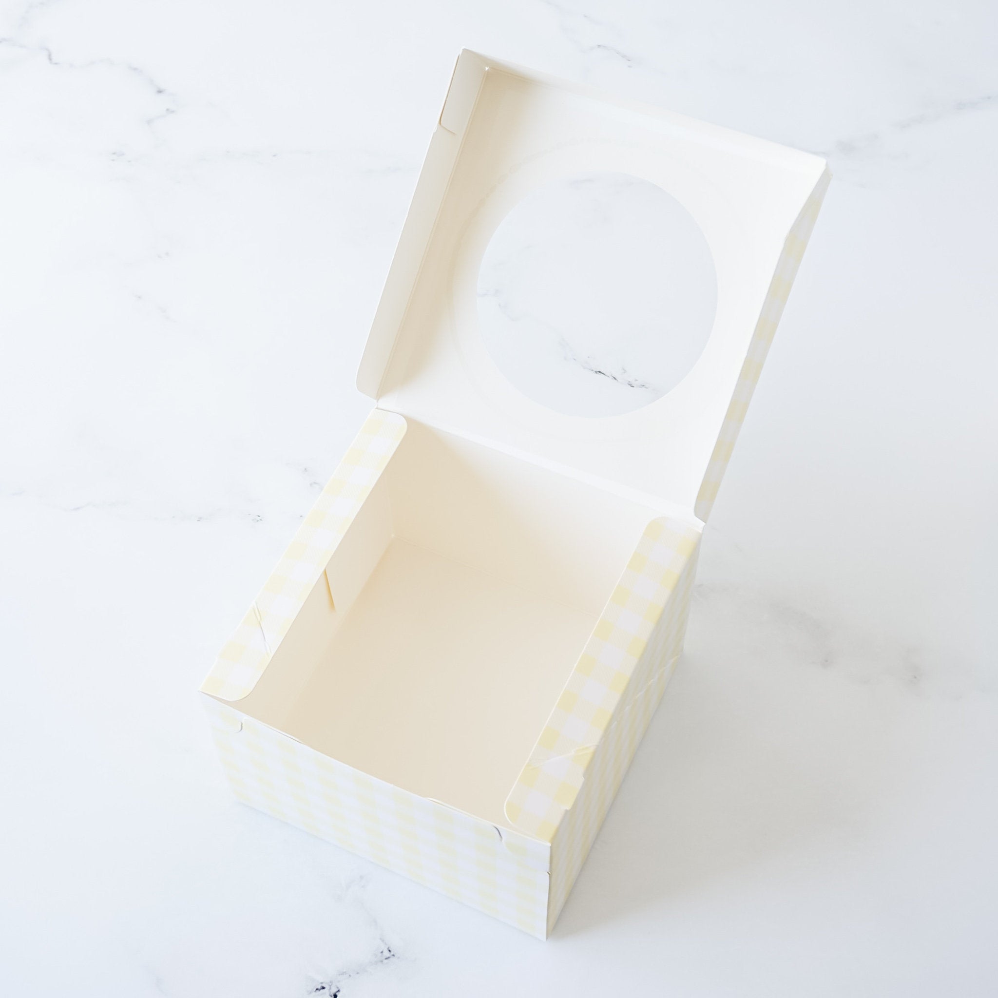 An open, empty, white cardboard box with a yellow and white checkered pattern. The box has a clear plastic window on the top.