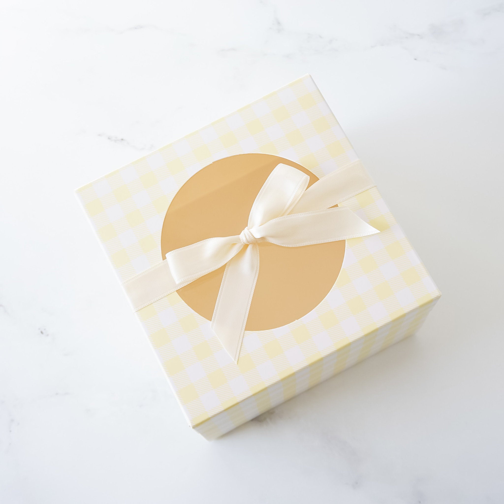 A yellow gingham cookie box with a round window on top, adorned with a satin bow.