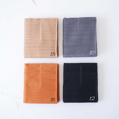 Four folded kitchencloths in beige, gray, orange, and black on a white background.