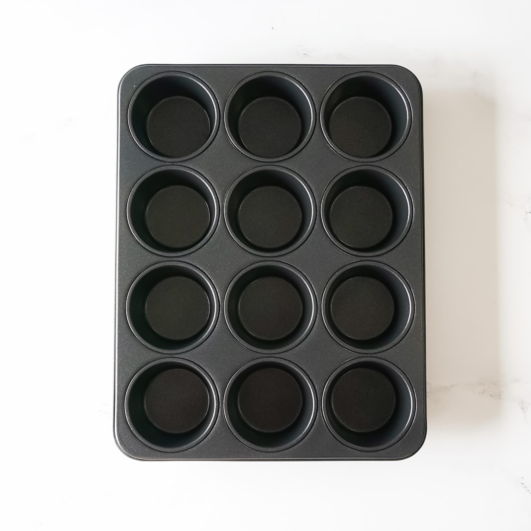 A black metal cupcake pan with 12 empty muffin cups.