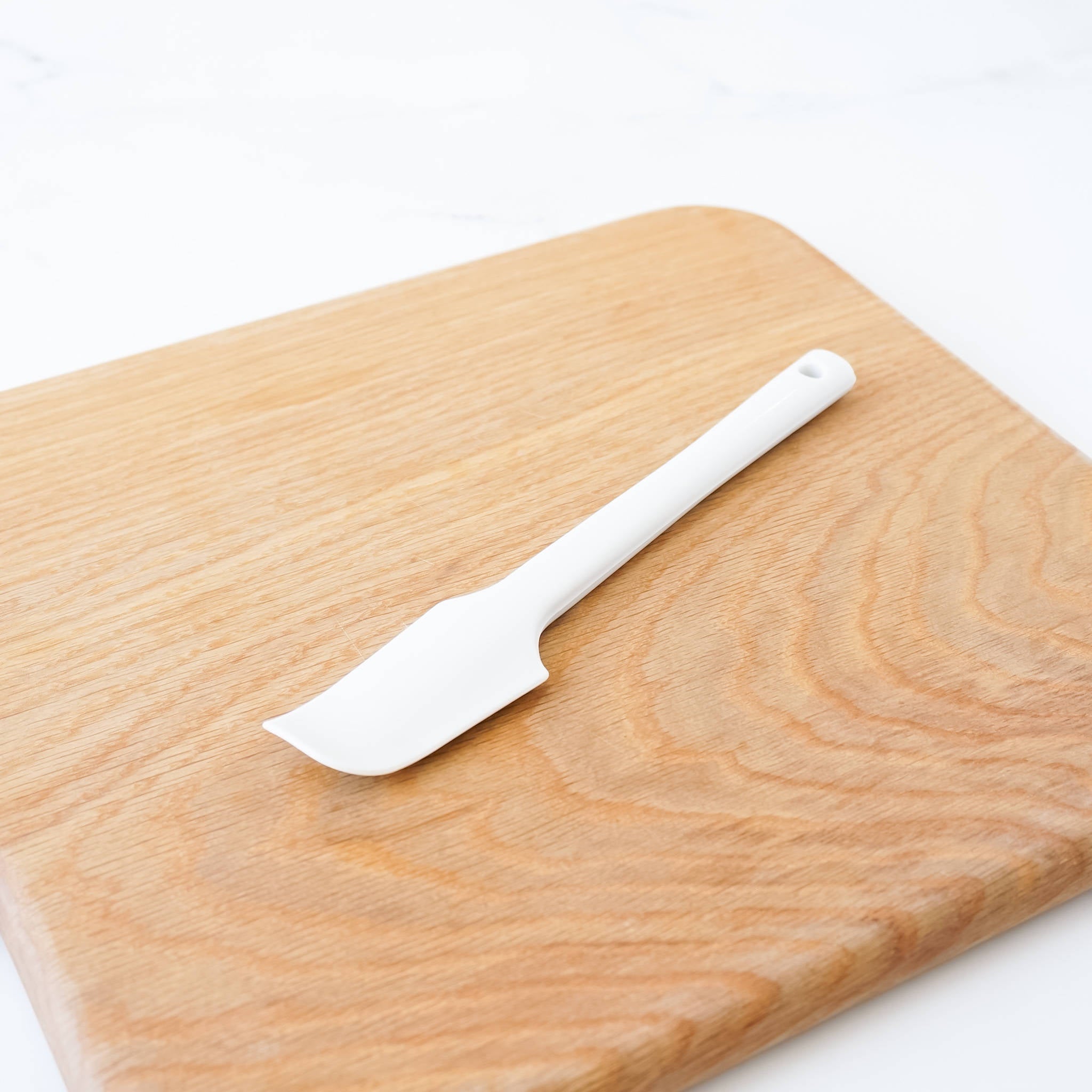 A white silicone spatula on a light brown wooden cutting board.