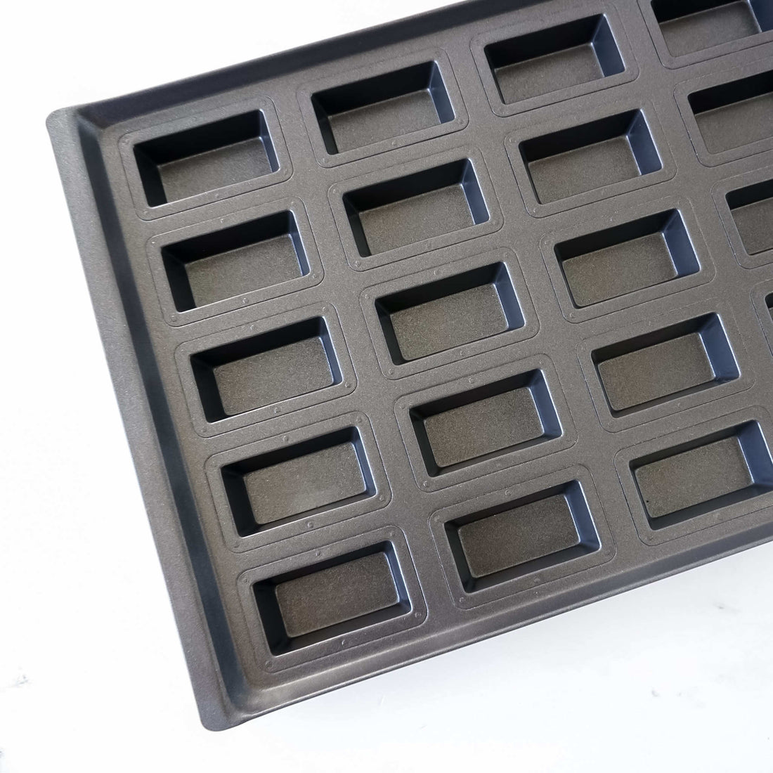 Black financier cake mold with multiple rectangular cavities on a white background