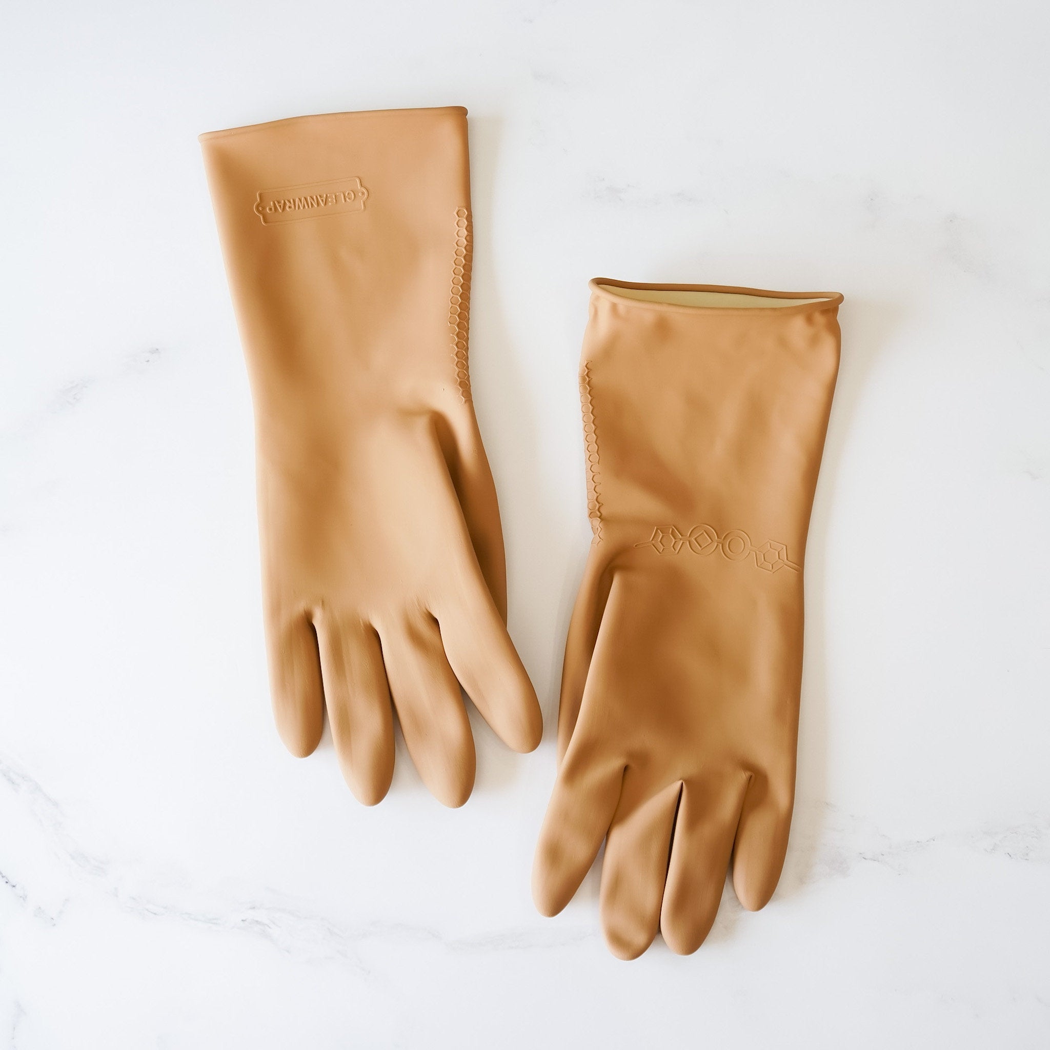 A pair of beige cleaning gloves placed on a marble surface, showing the front and back sides with subtle embossed patterns.