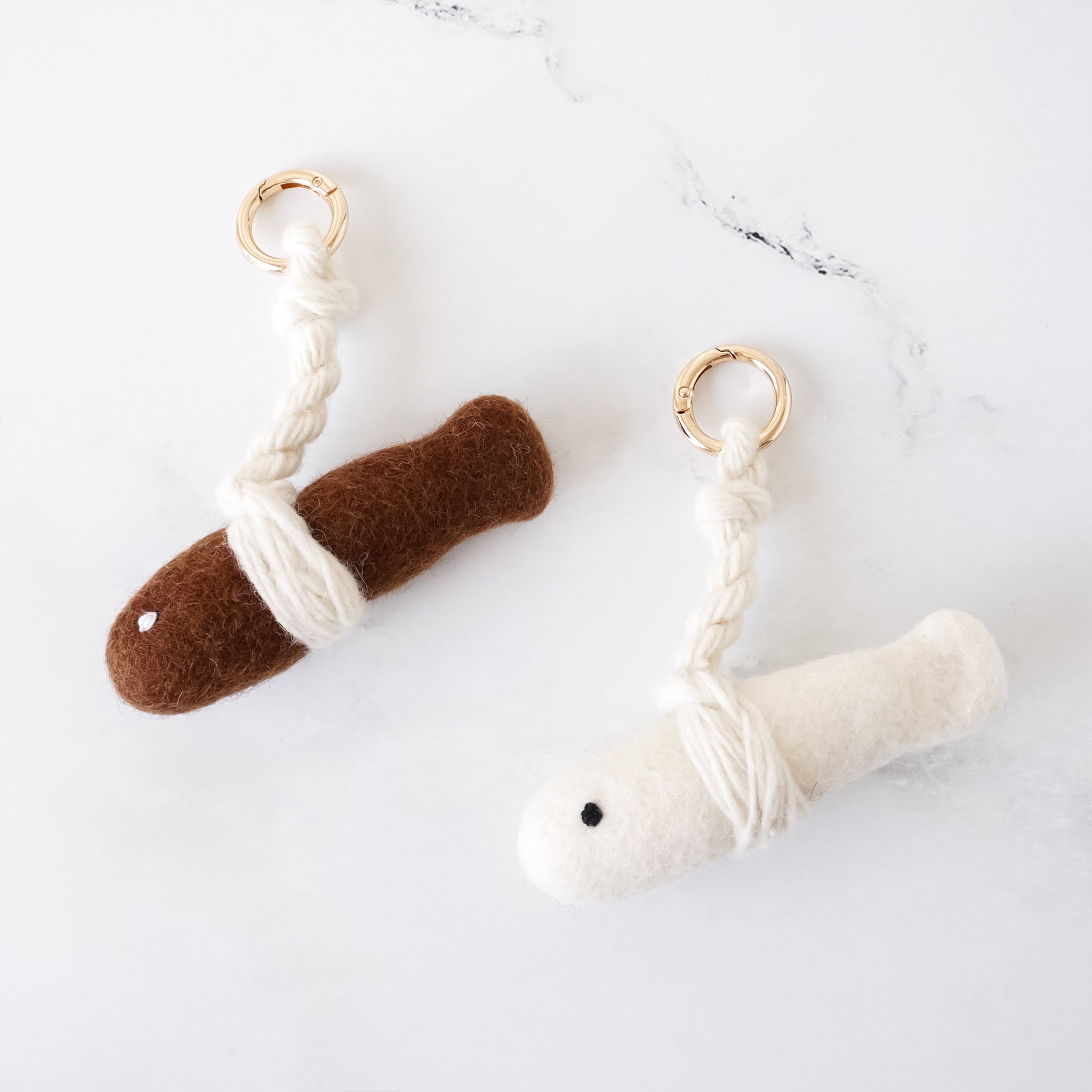 Two keychains, one brown and one white, on a marble surface.