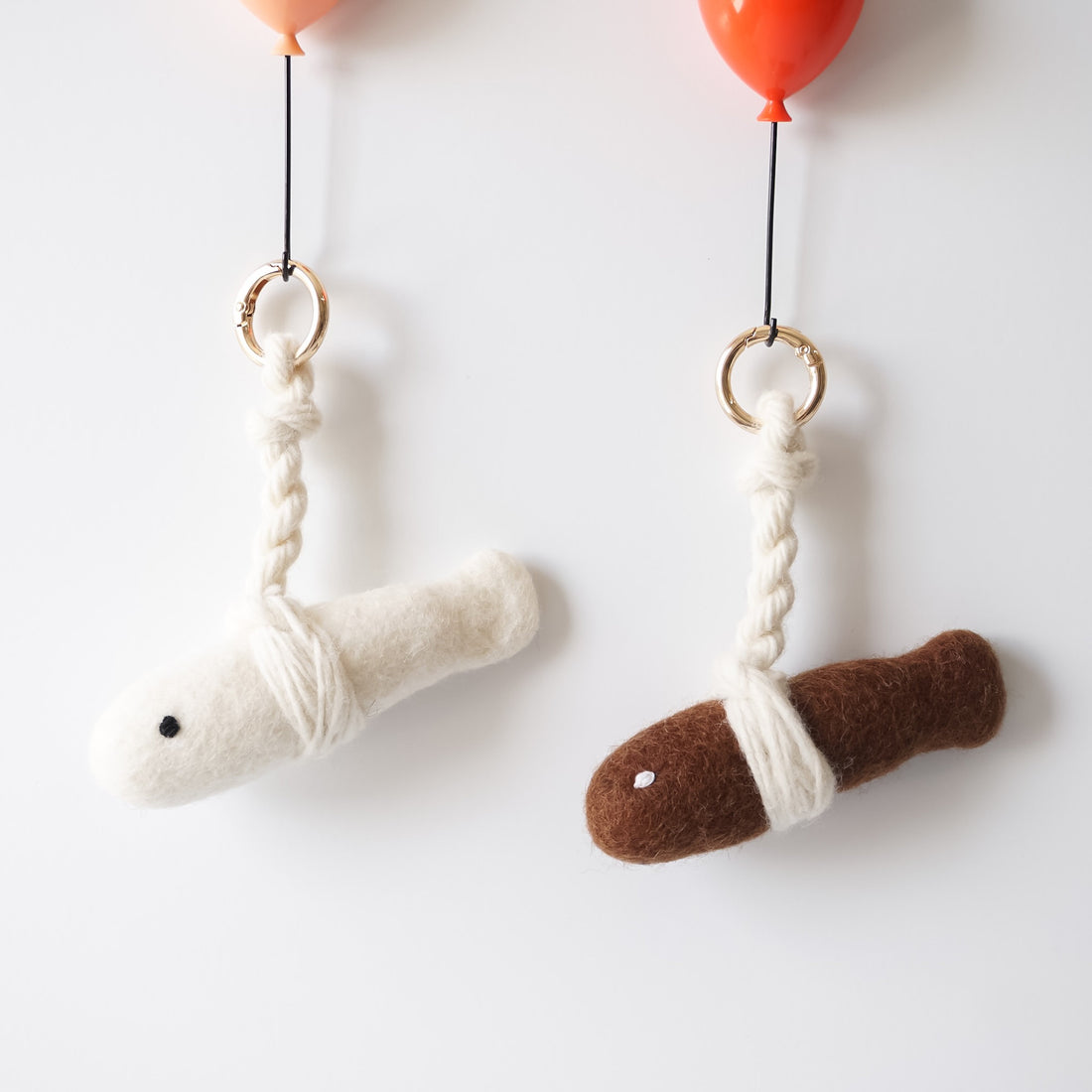 Two felted fish key rings hanging from balloons on a white background