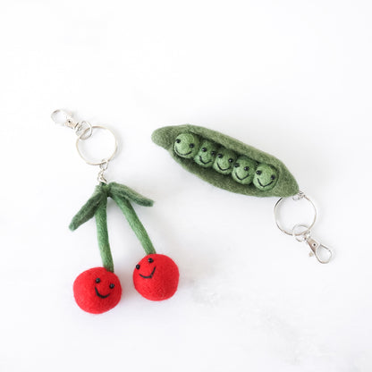Felt keychains shaped like cherries and a green pea pod on a white background