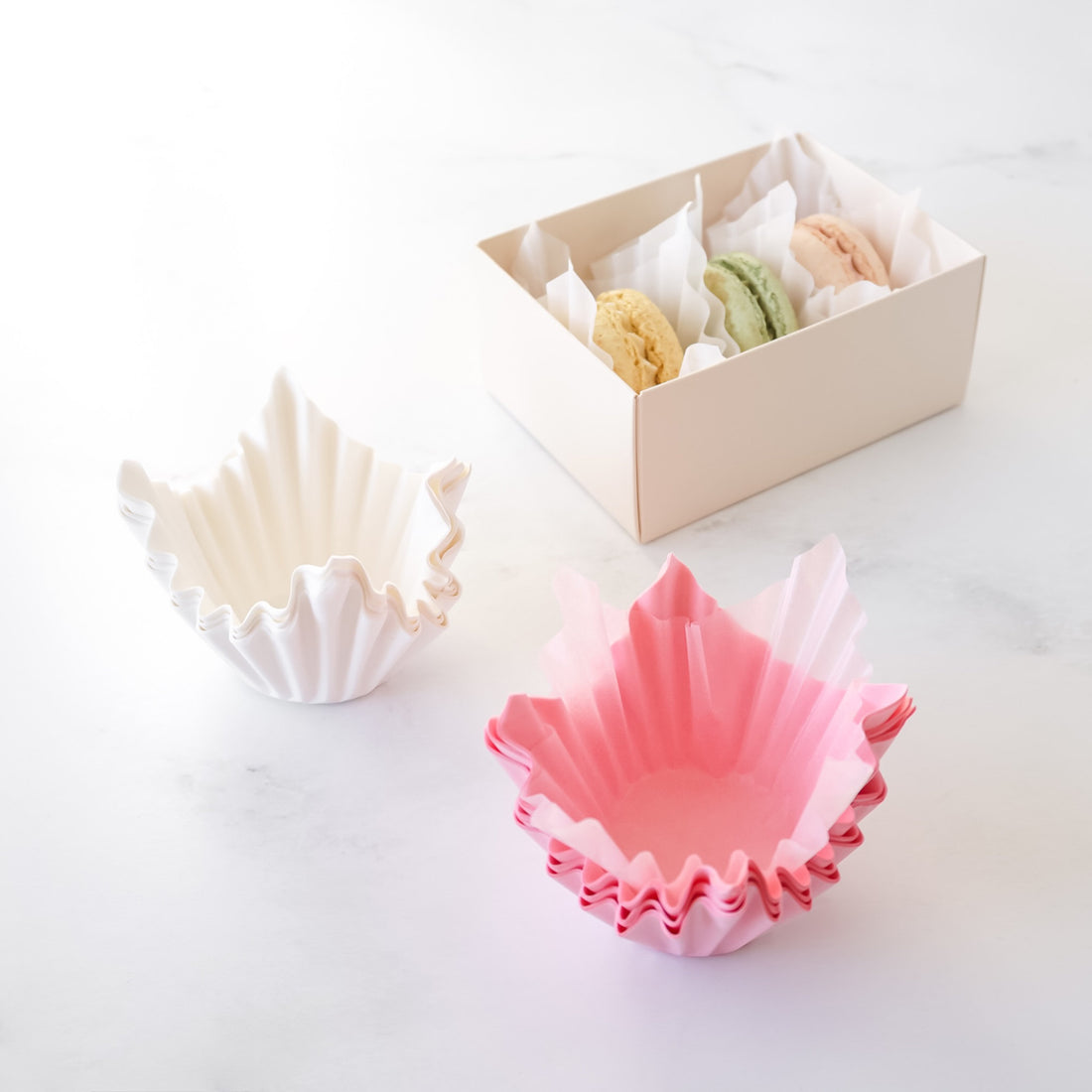 Colorful shell-shaped baking liners on a white surface with a box in the background.