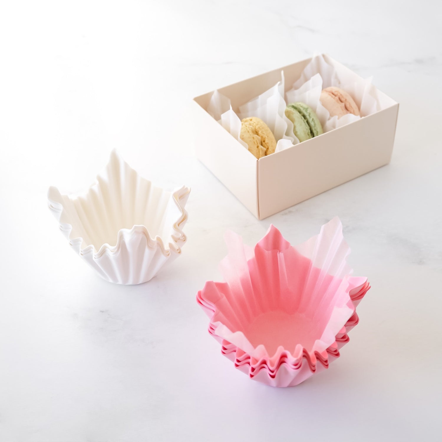 Colorful shell-shaped baking liners on a white surface with a box in the background.