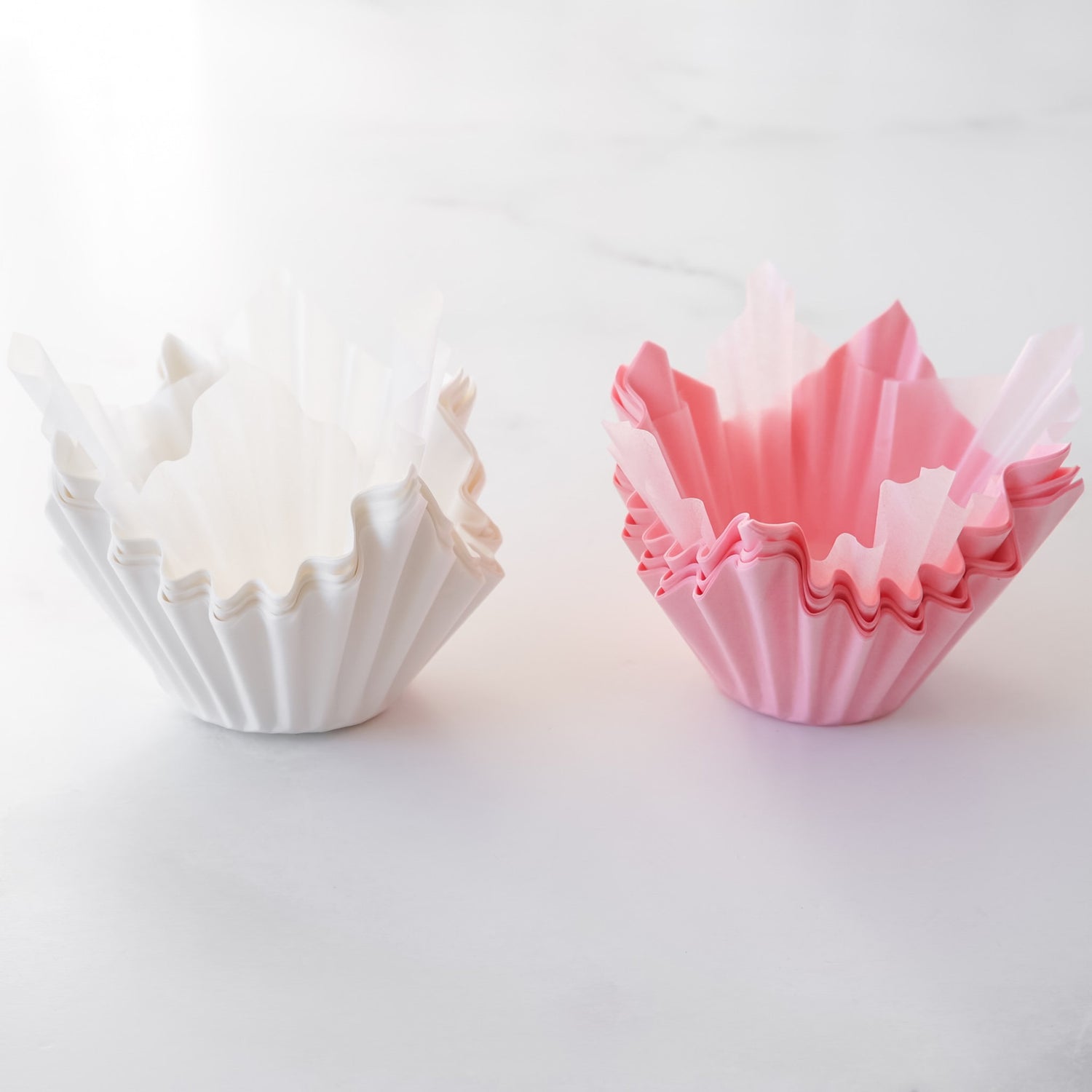 Two cupcake liners, one white and one pink, on a light gray background.
