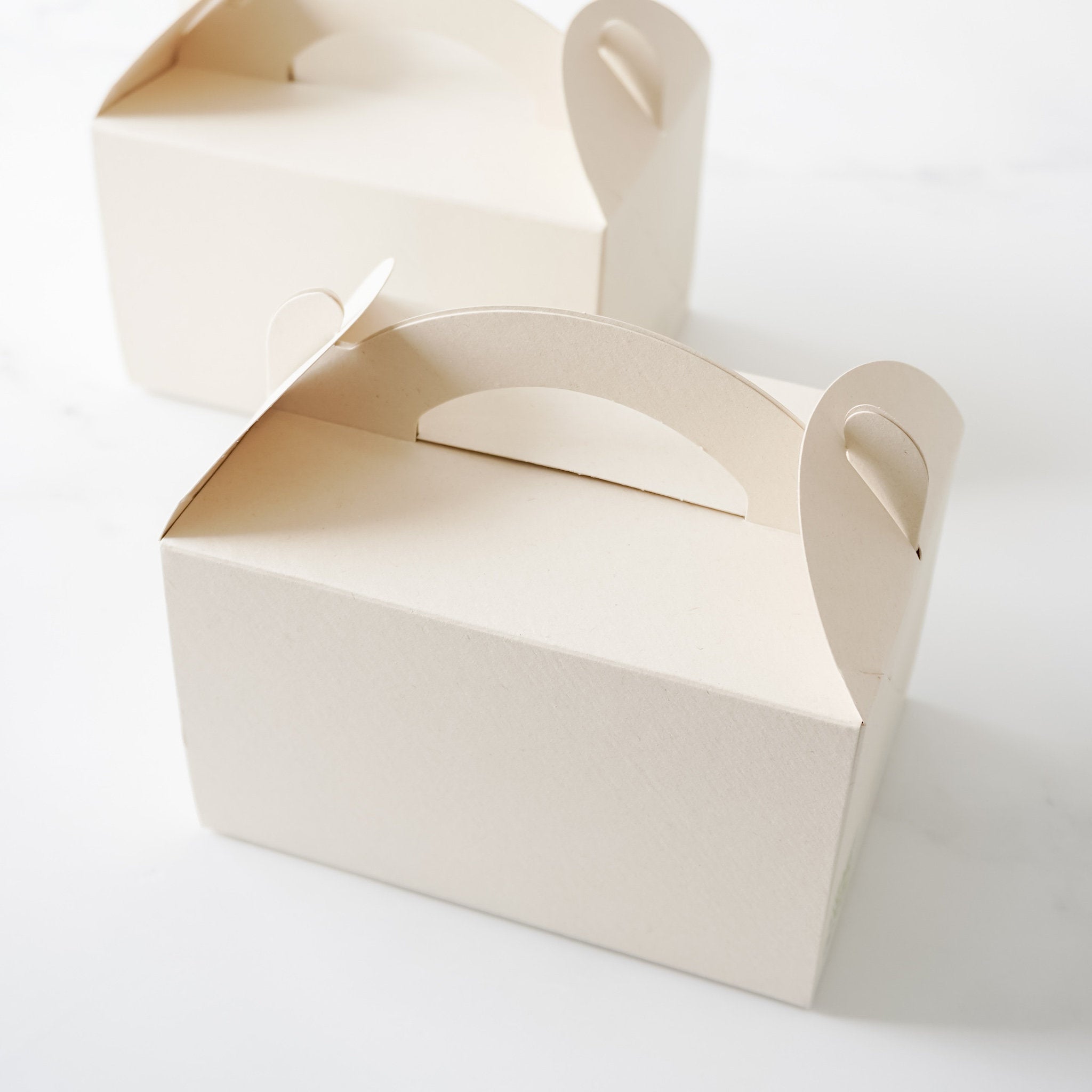 Two light beige cardboard boxes with cut-out handles. The boxes are empty and have a textured surface.