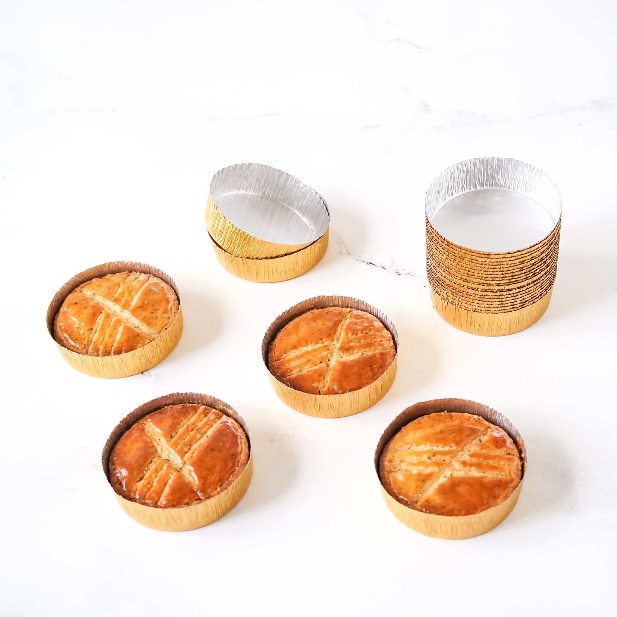 Gold aluminum foil molds arranged on a white surface, designed for baking Galette Bretonne, with some molds containing baked cookies.