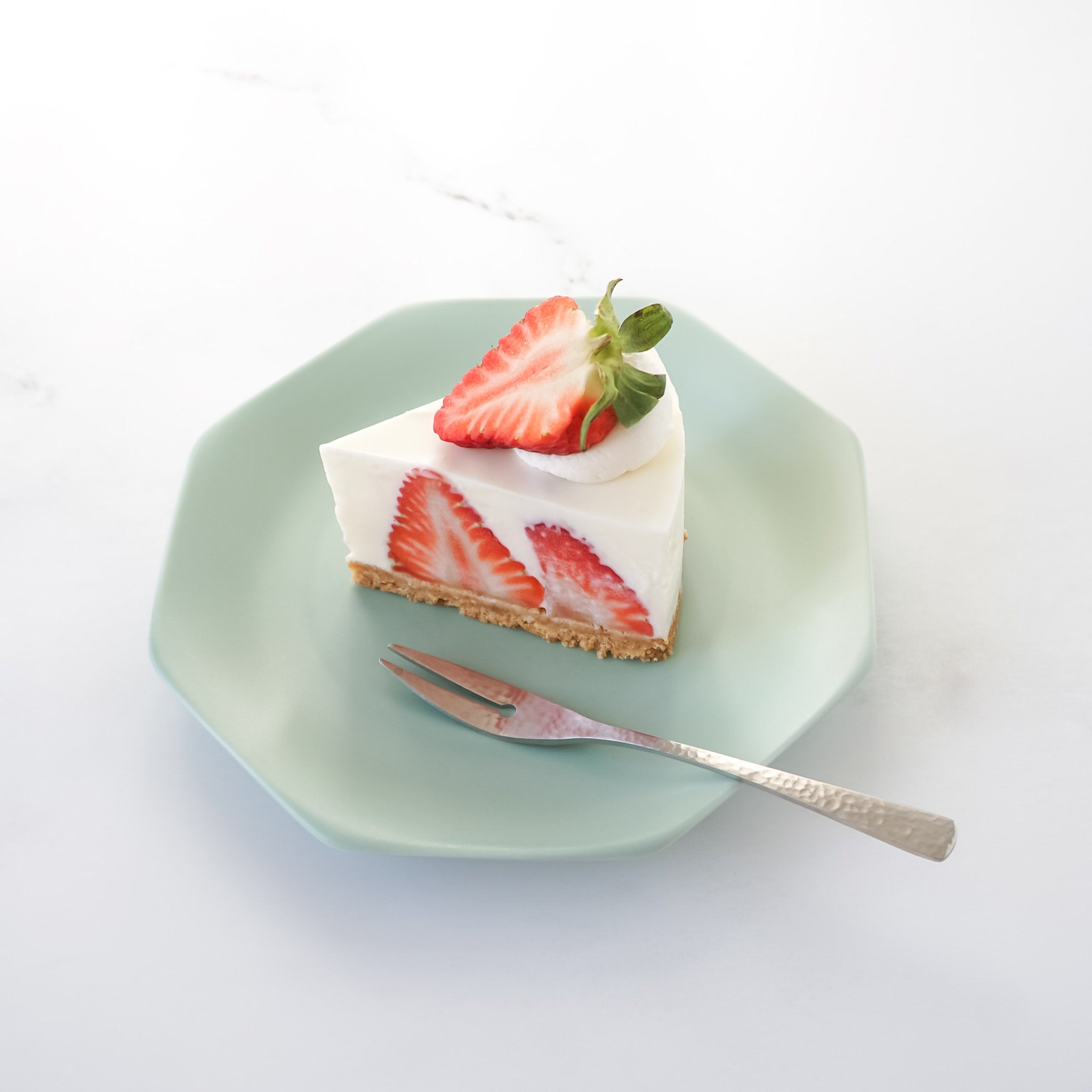 Slice of strawberry cheesecake on a green plate with a fork on a white background
