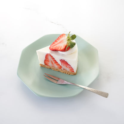 Slice of strawberry cheesecake on a green plate with a fork on a white background