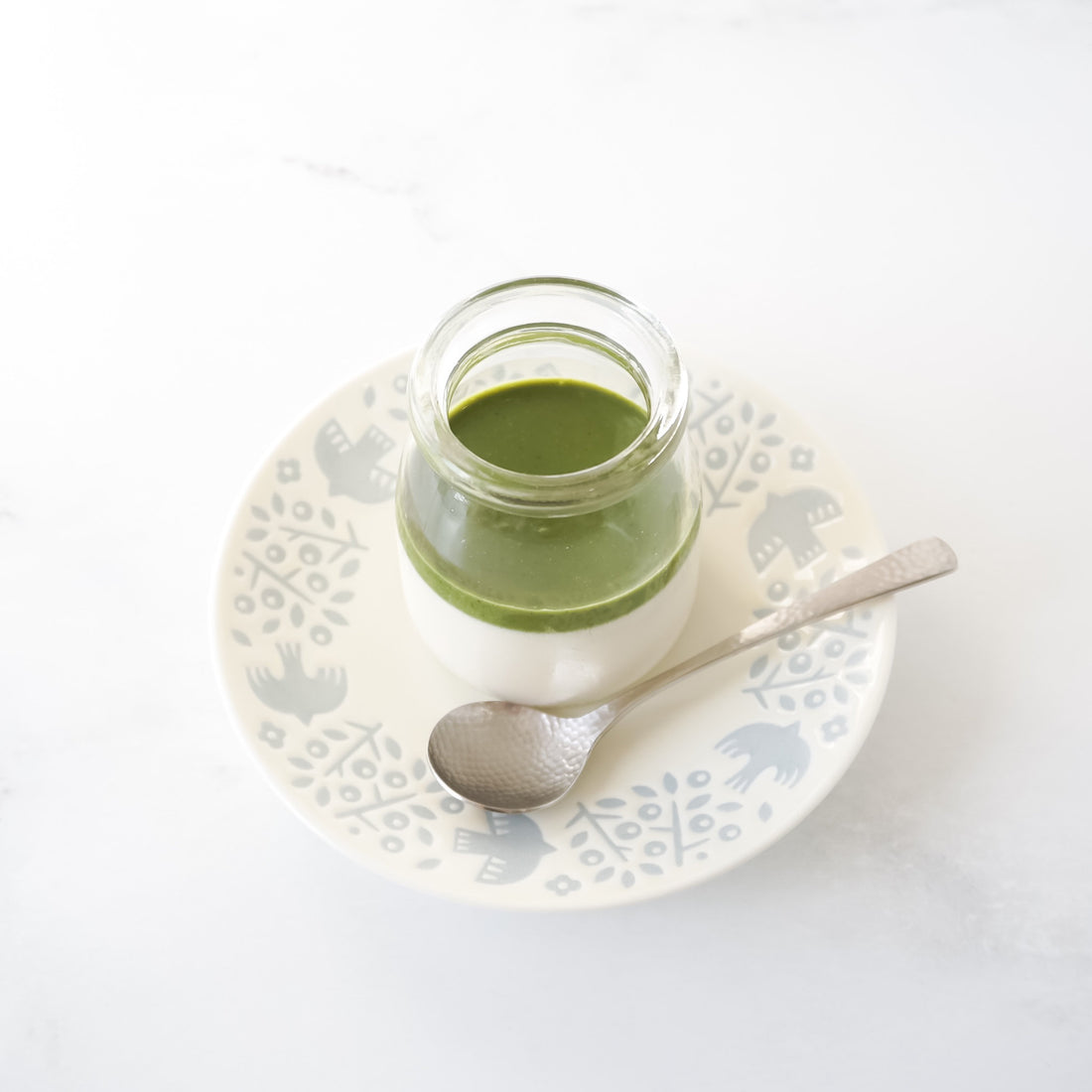 Jar of matcha panna cotta on a decorative plate with a spoon