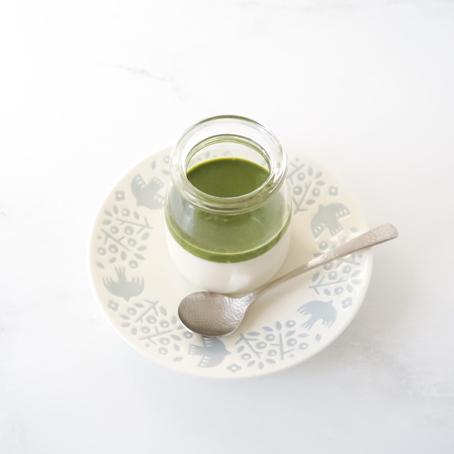 Jar of matcha panna cotta on a decorative plate with a spoon