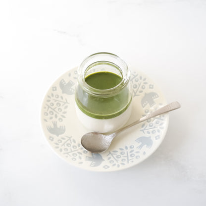 Jar of matcha panna cotta on a decorative plate with a spoon