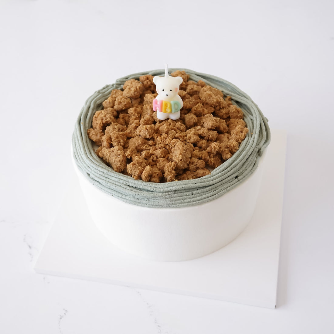 A birthday cake with crumbled top and a small bear candle on a white background