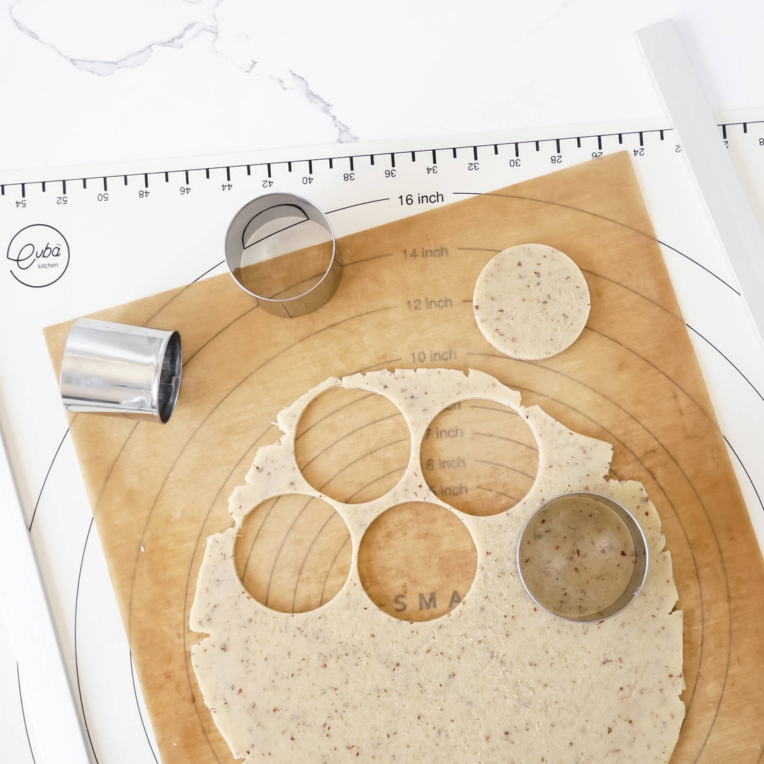 Stainless steel cookie cutter with circular shapes on a silicone mat with a ruler in the background.