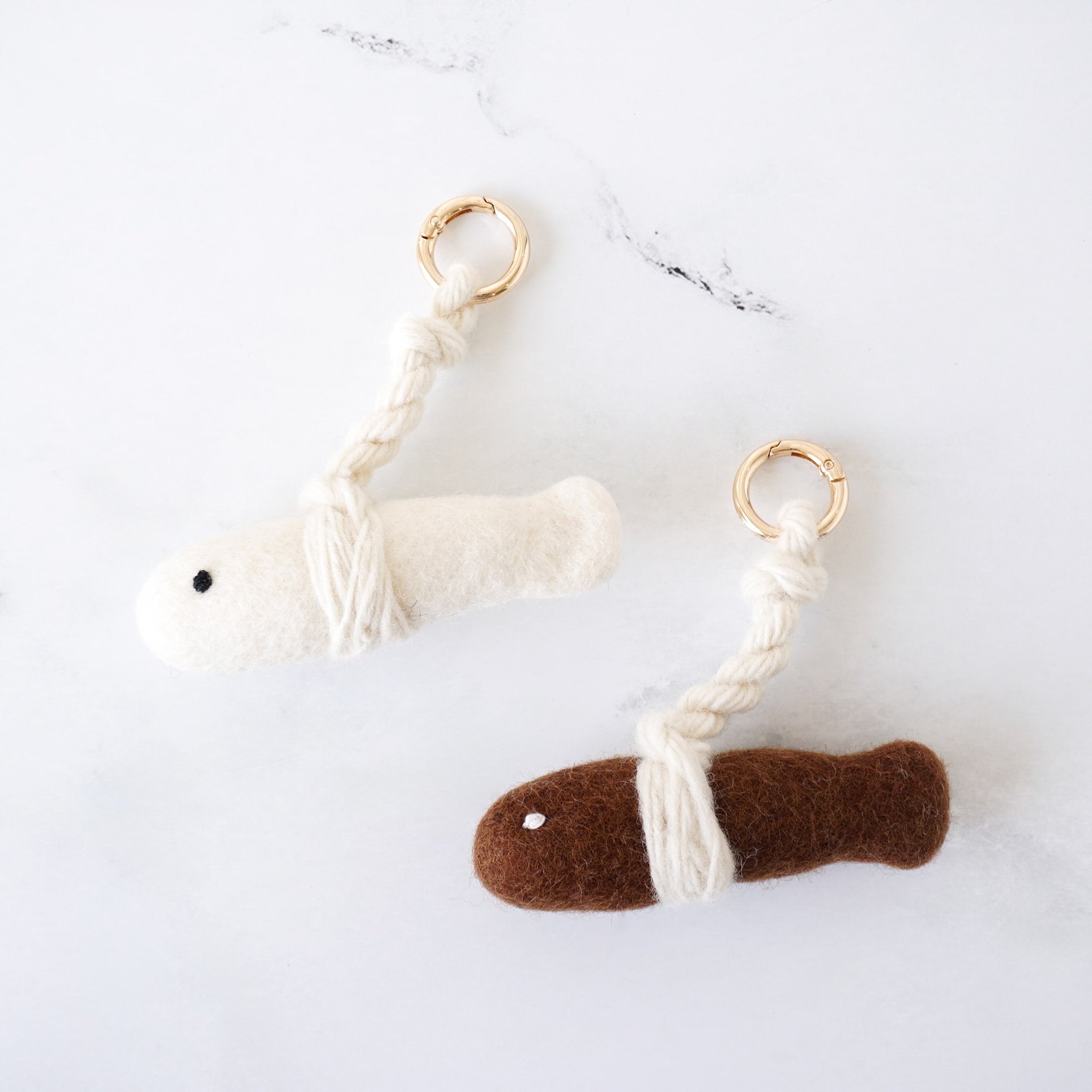 Two fish keychains, one white and one brown, on a marble surface.