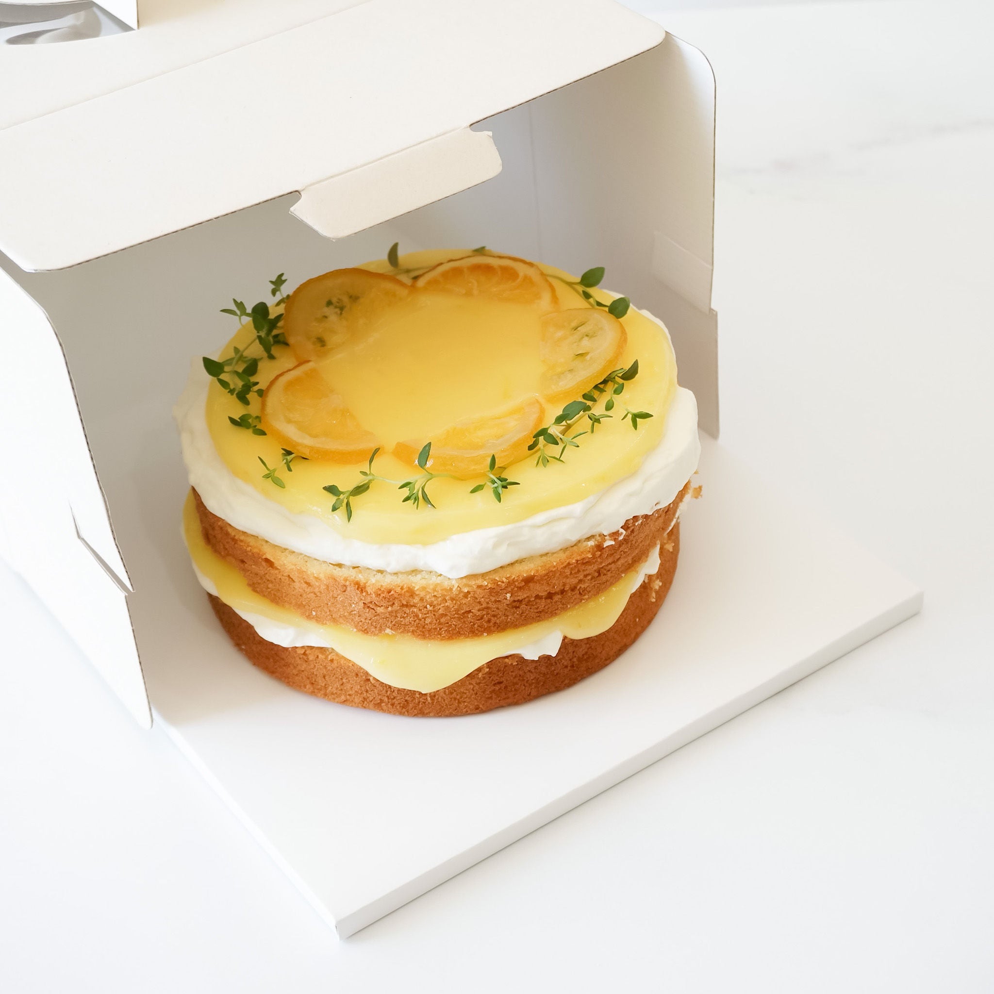A lemon curd cake presented on a white square cake board with a matte finish.