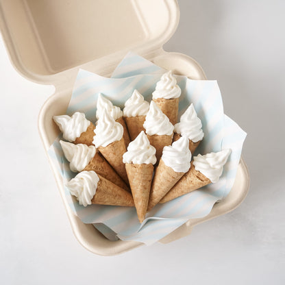 Mini meringue cookies shaped like ice cream cones in a beige container on a light gray background
