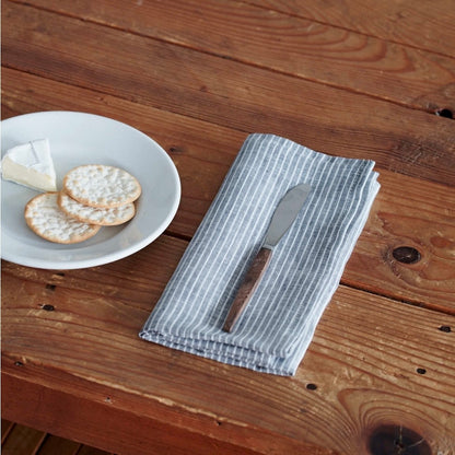 Napkin with a knife on a wooden table next to a plate of cheese and crackers