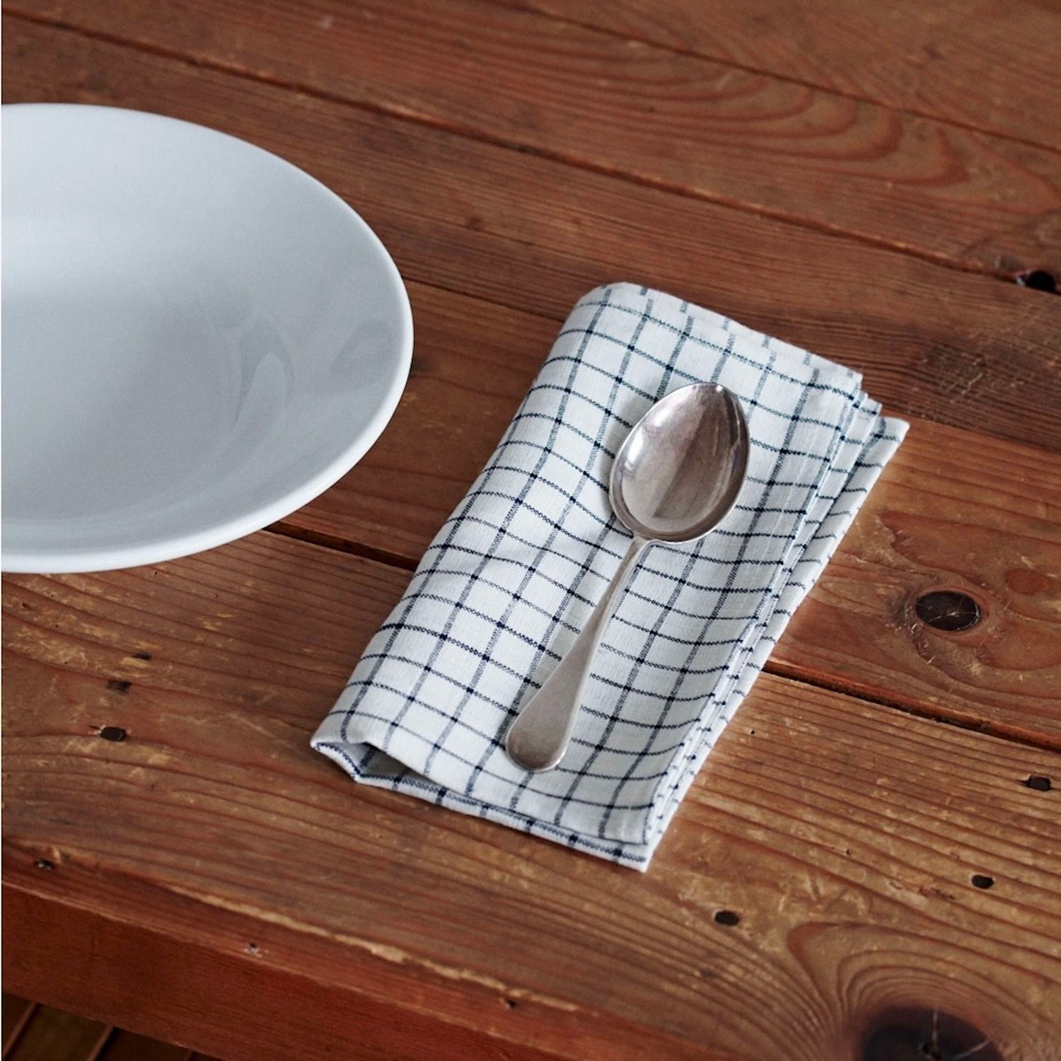 Spoon on a checkered cloth with a white bowl on a wooden surface